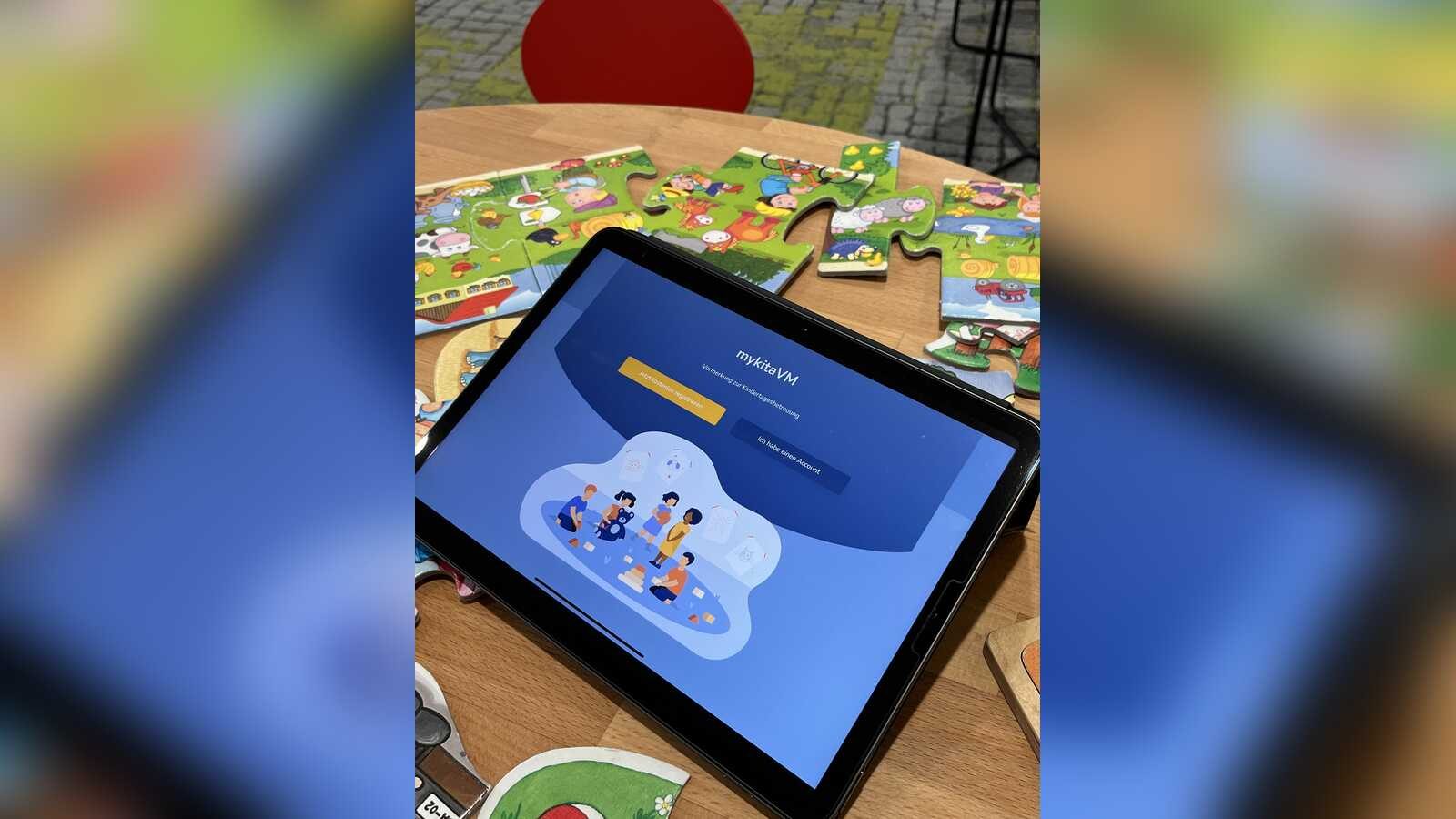 Tablet mit geöffnetem Online-Elternportal zur Kita-Anmeldung auf einem Tisch mit Kinderpuzzles
