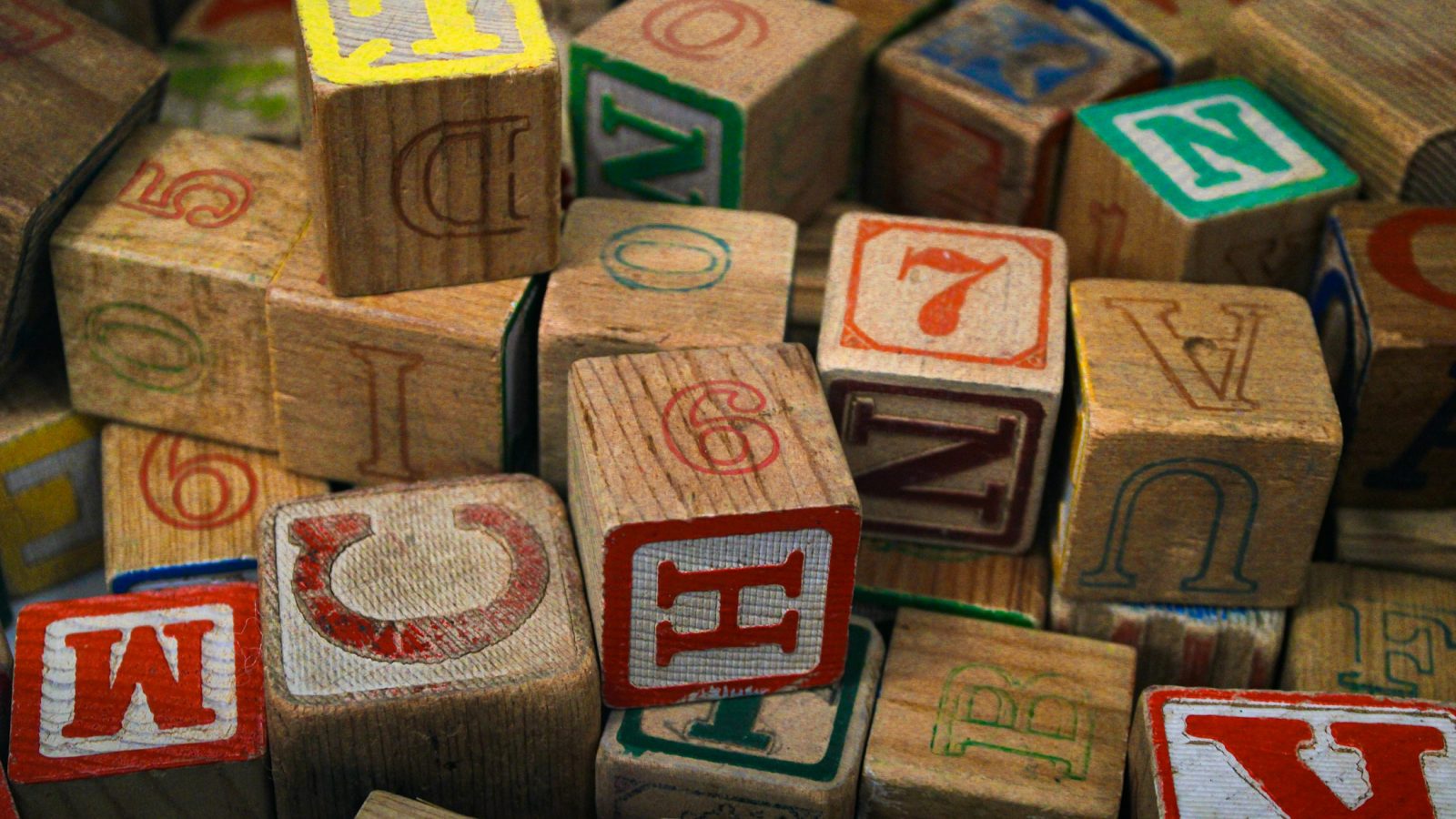 Bunte Holzbuchstaben-Bausteine aufgestapelt (Symbolbild)