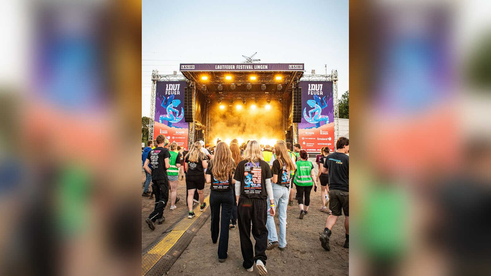 Helfer in Festival-T-Shirts gehen auf die beleuchtete Hauptbühne des LAUTFEUER Festivals in Lingen zu