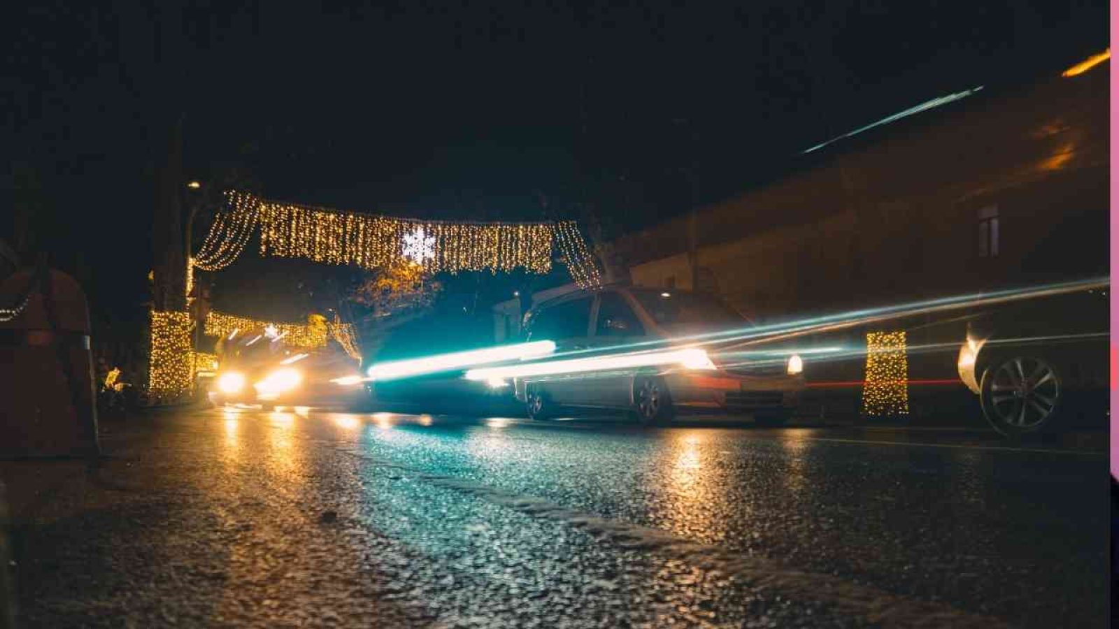 Autos fahren unter einer festlichen Beleuchtung mit Lichtern und Dekorationen auf einer Straße bei Nacht.
