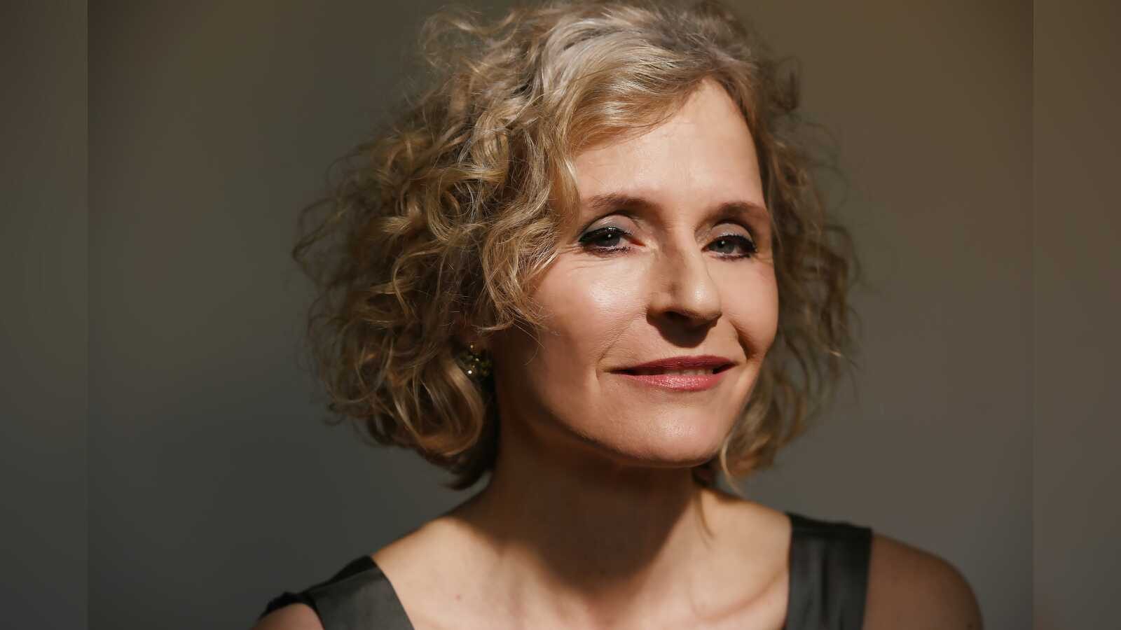 Porträt von Maria Vollmer mit lockigem blondem Haar vor grauem Hintergrund