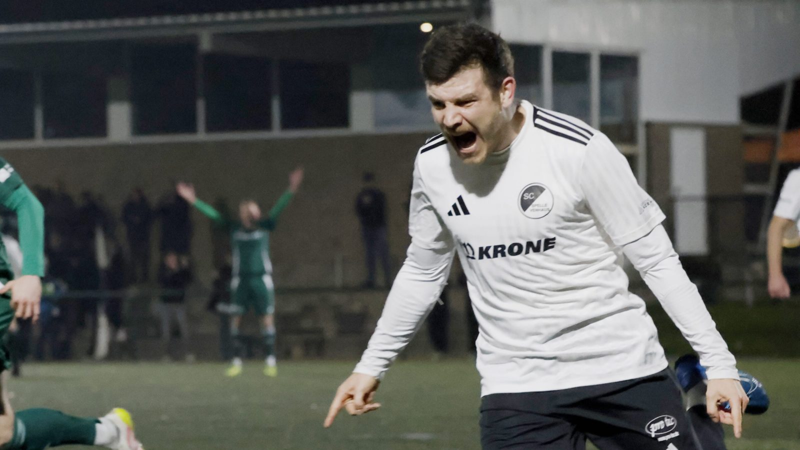 Fußballspieler in weißem Trikot, der nach einem Tor jubelt, während andere Spieler im Hintergrund agieren.