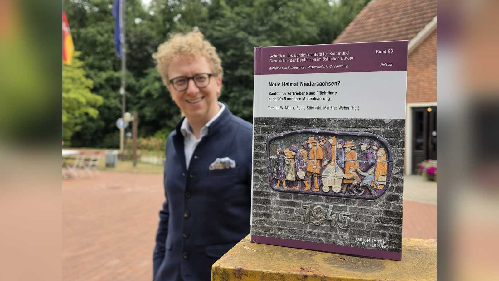 Museumsdirektor Dr. Torsten W. Müller hält den neuen Sammelband Neue Heimat Niedersachsen in den Händen