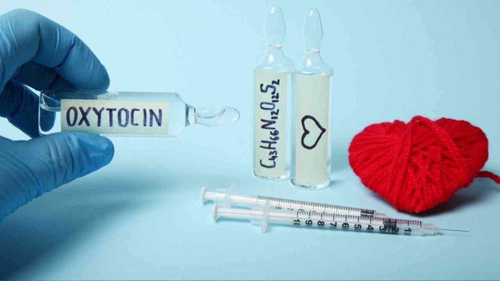 Ampulle mit Oxytocin und zwei weiteren Ampullen sowie einer Spritze und einem roten Herz aus Garn.