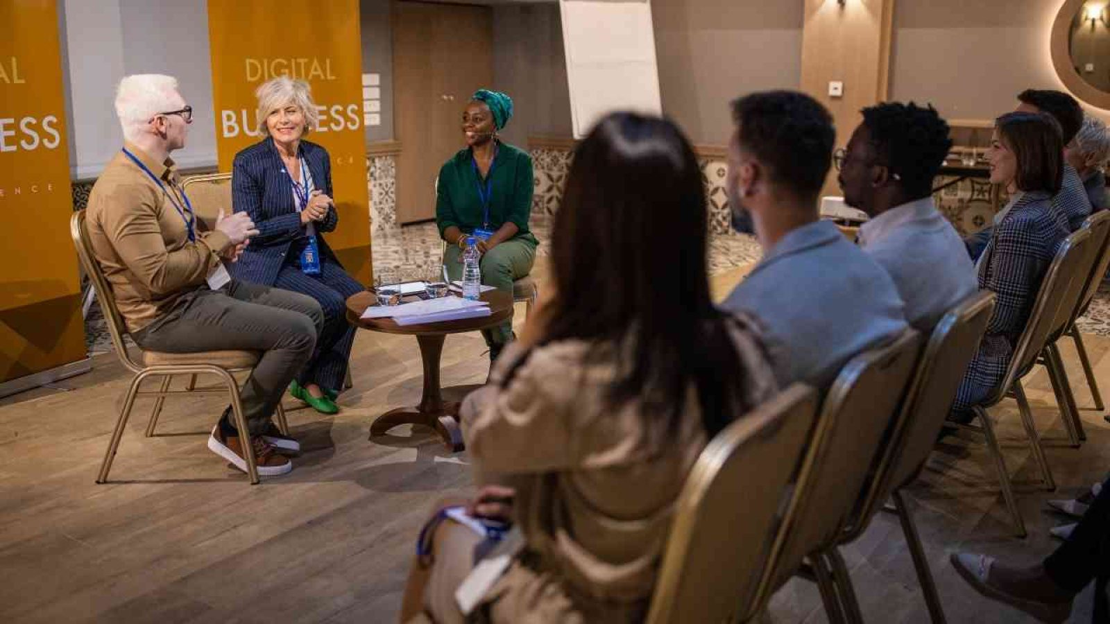 Podiumsdiskussion mit mehreren Teilnehmern in einem modernen Veranstaltungsraum.