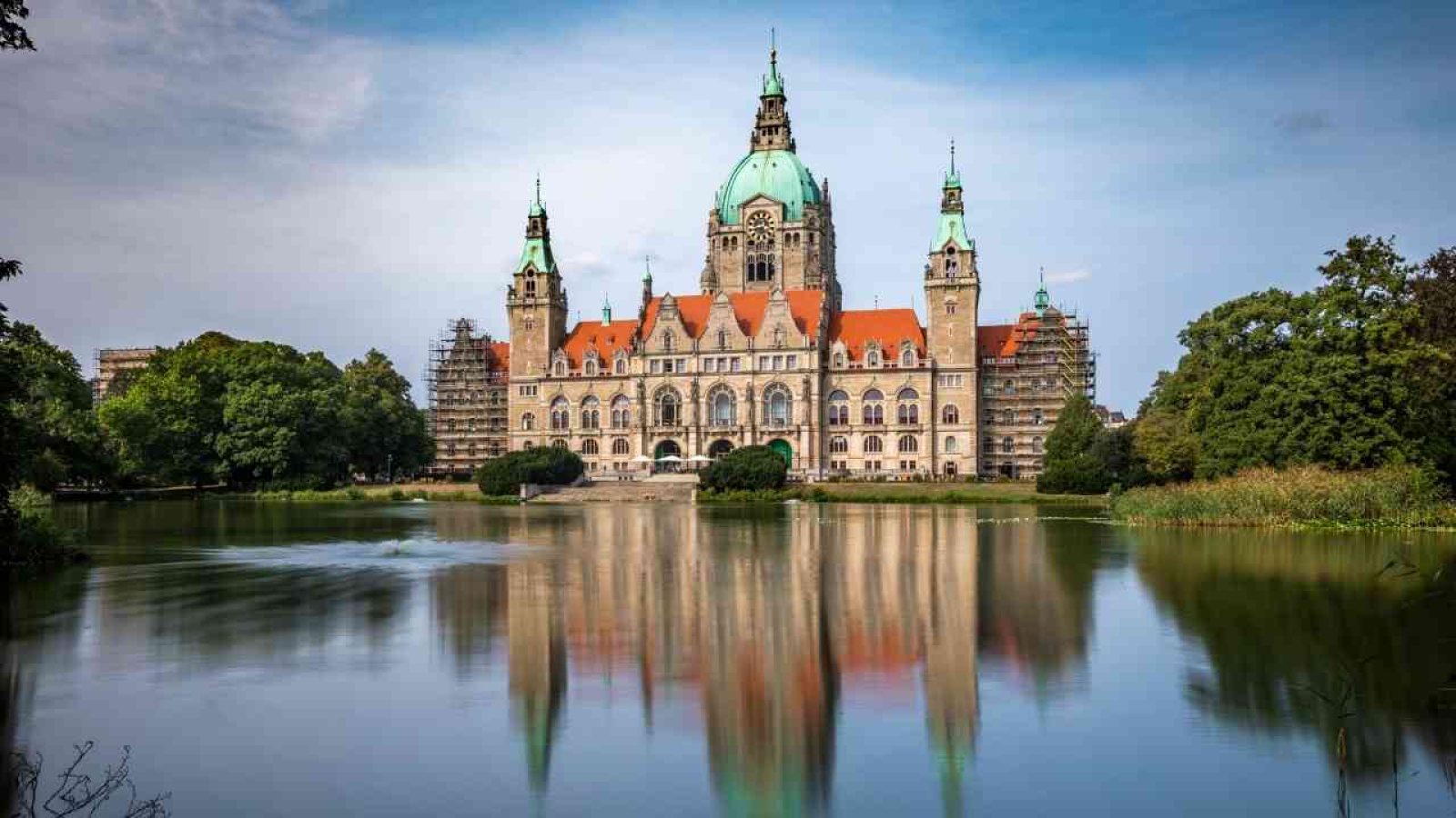 Rathaus Niedersachsen mit grüner Kuppel und reflektierendem Wasser im Vordergrund.
