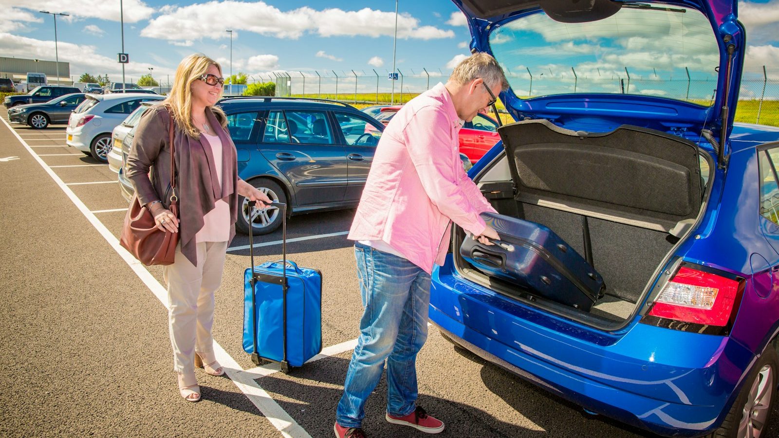 Paar verstaut Koffer im Auto – Symbolbild für Urlaubsreisen