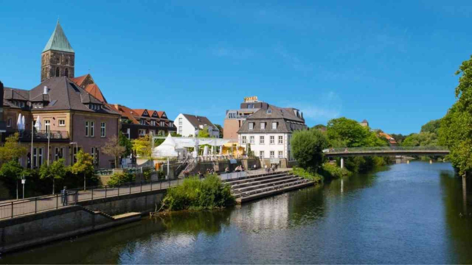Blick auf das Wasser mit Gebäuden und Bäumen entlang des Ufers in Rheine.