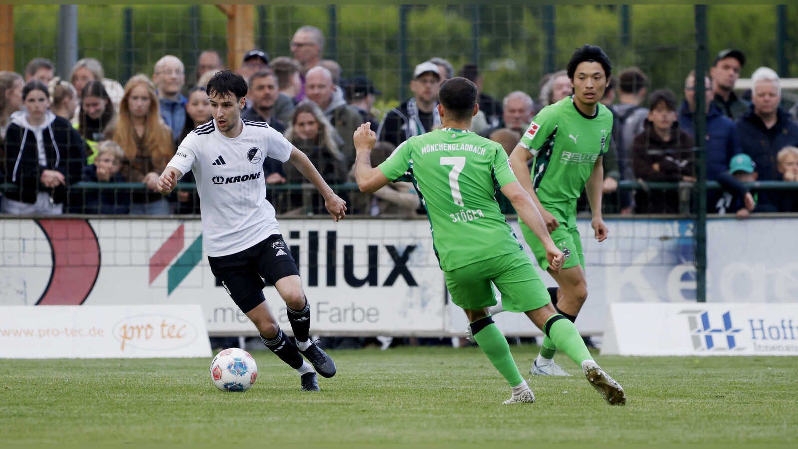 Anton Popov vom SC Spelle-Venhaus im weißen Trikot am Ball, zwei Gegenspieler in Grün laufen auf ihn zu