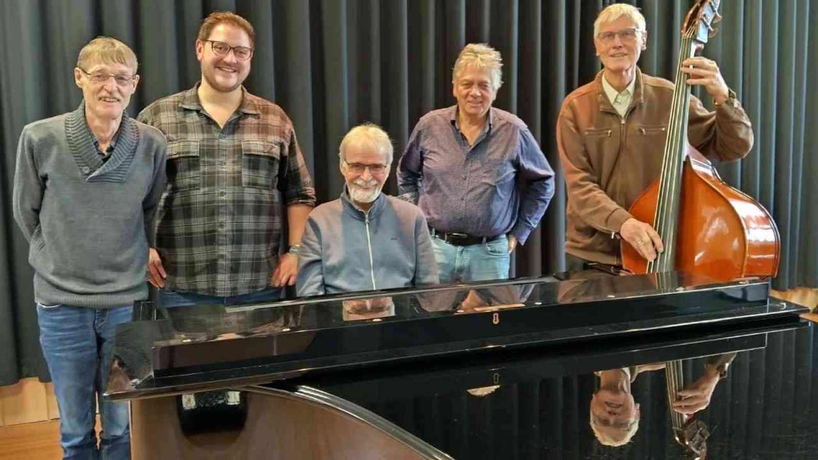 Fünf Männer posieren mit Klavier und Kontrabass in einem Musikraum. Eine musikalische Gruppe.