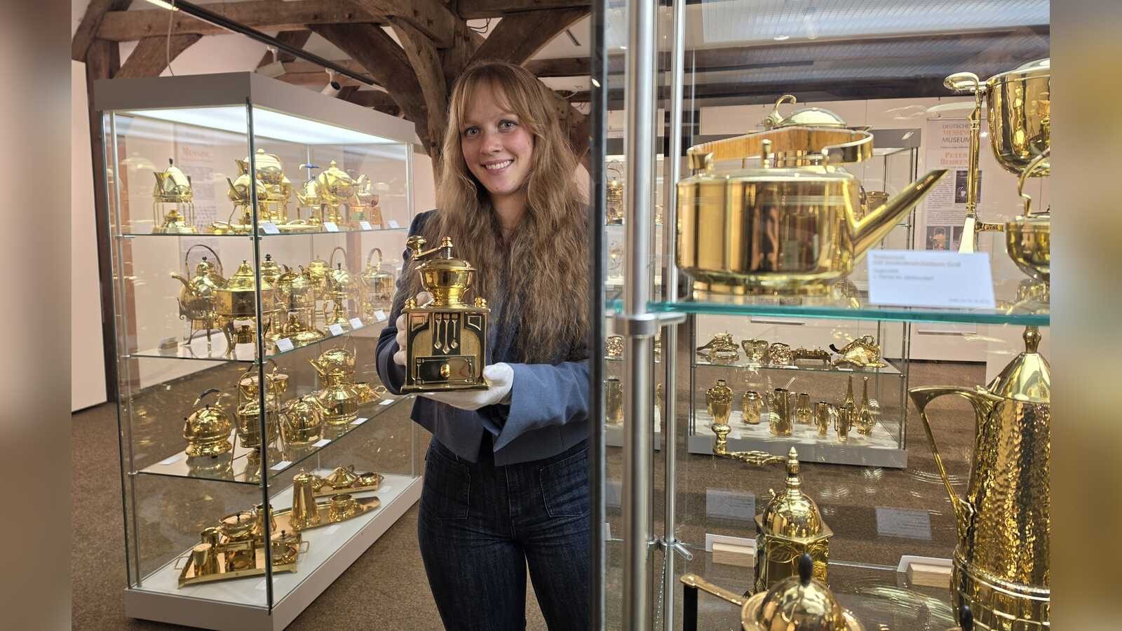 Volontärin Judith Middendorf mit einer Kaffeemühle aus Messing in der Ausstellung Schimmernde Schönheiten