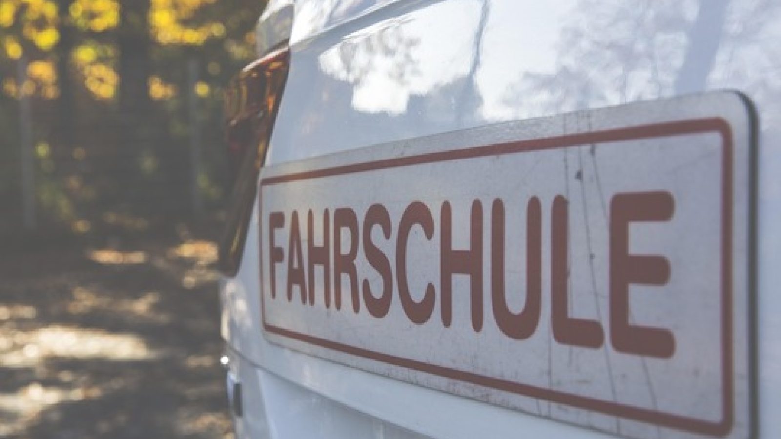 Nahaufnahme eines Fahrzeugs mit dem Aufkleber 'FAHRSCHULE' auf der Seite, das in einem Außenbereich steht.