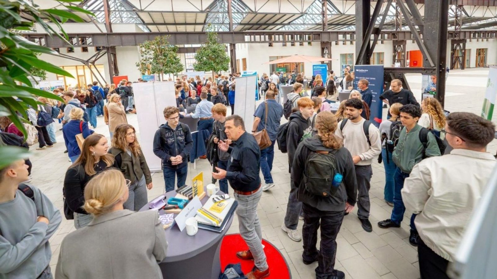 Menschen bei einer lebhaften Messe in einer modernen Halle, die an Ständen Informationen austauschen und Netzwerke knüpfen.