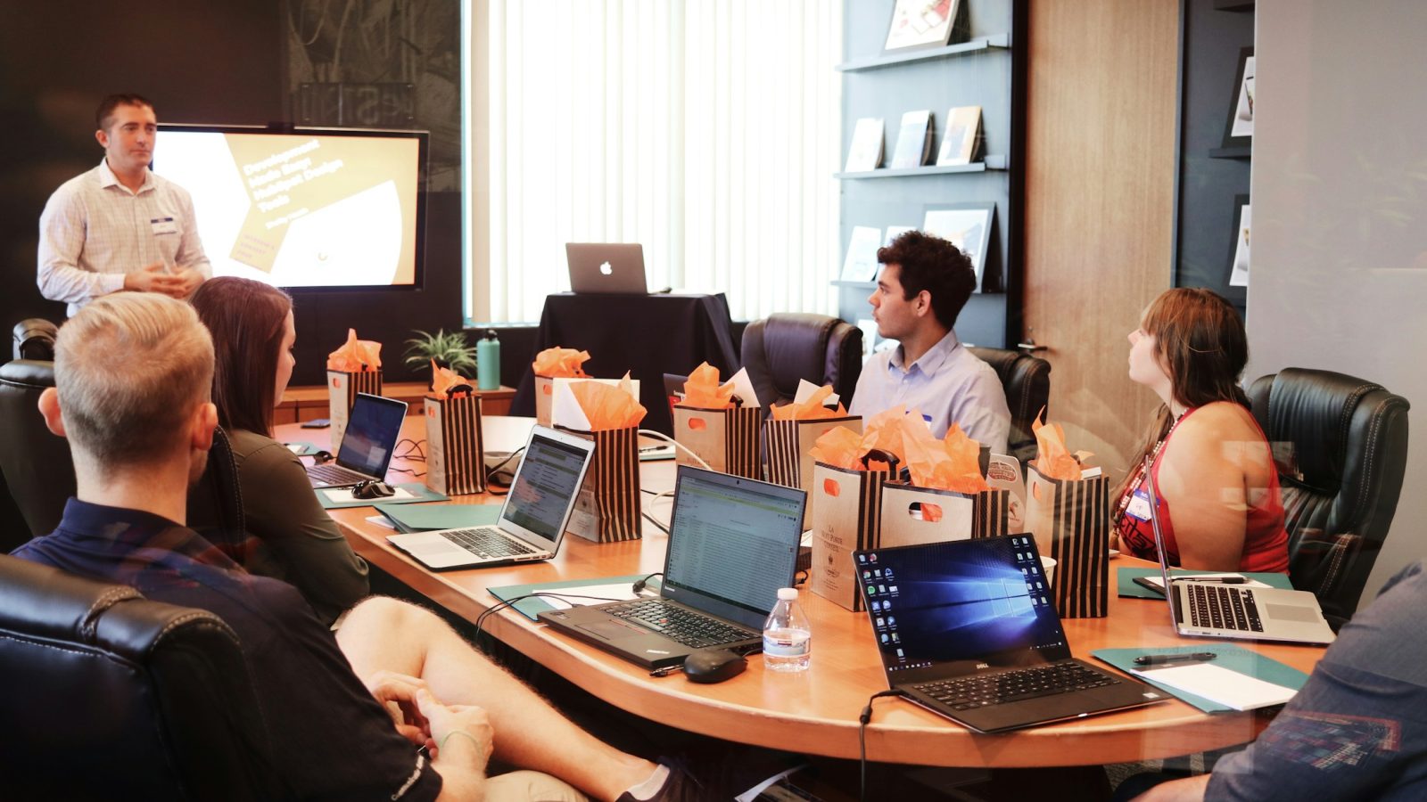 Ein Referent spricht vor Teilnehmenden, die mit Laptops an einem Tisch sitzen