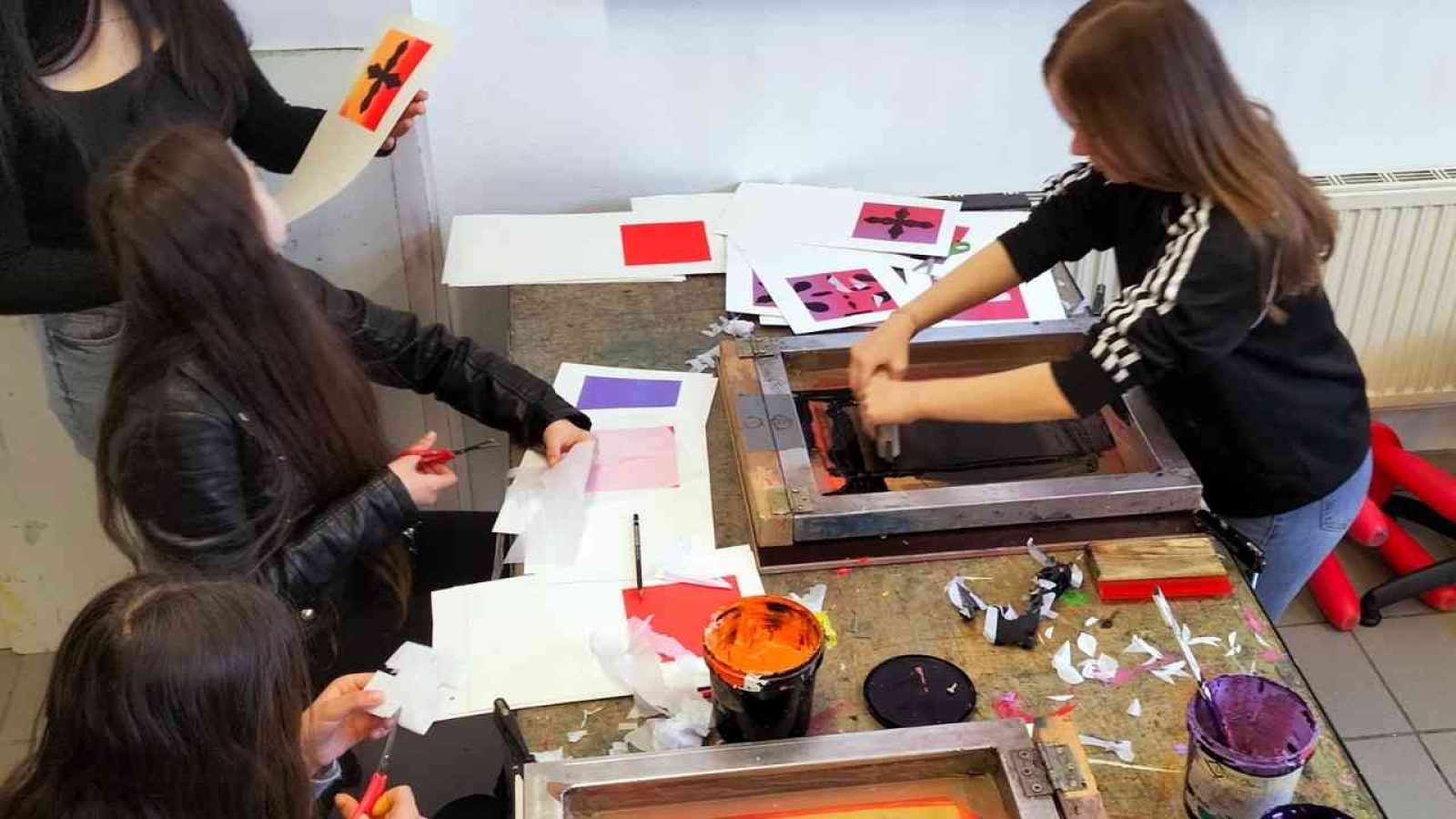Kinder beim kreativen Siebdruck-Workshop, gestalten bunte Motive auf Papier mit Farbe und Schablonen.