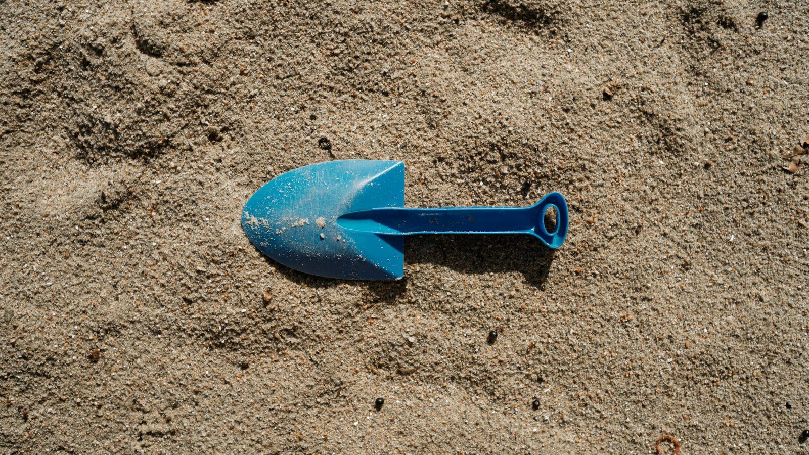 Blaue Spielzeugschaufel steckt im Sand
