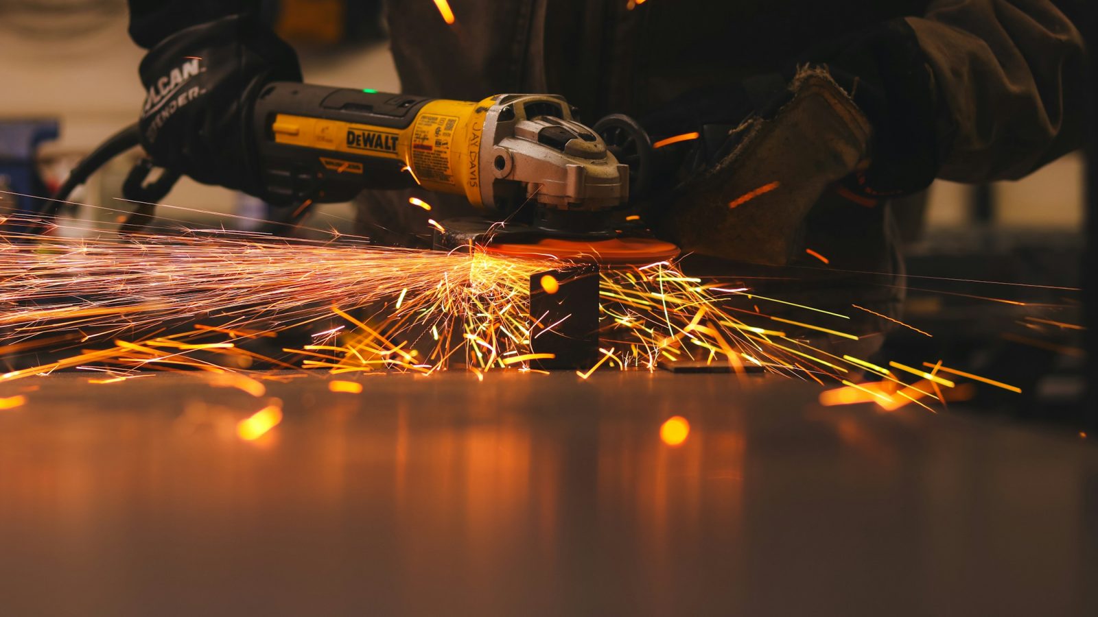 Ein Mann bearbeitet in einer Werkstatt ein Metallteil mit einem Winkelschleifer, Funken sprühen