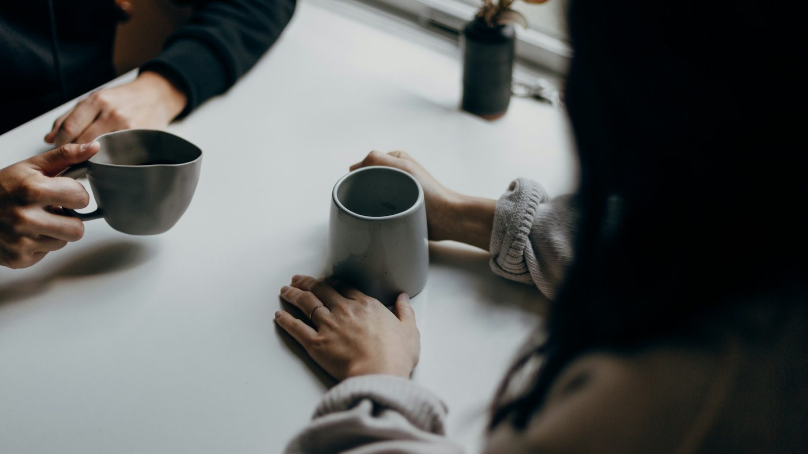 Zwei Personen mit Kaffeebechern im Gespräch an einem Tisch, Symbolbild für Streitschlichtung