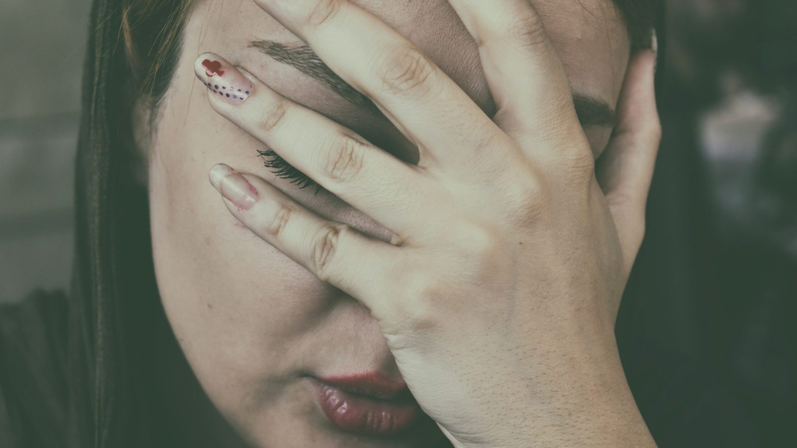 Frau hält sich schmerzbedingt die Hand ans Gesicht, Symbolbild für Migräne und Kopfschmerz