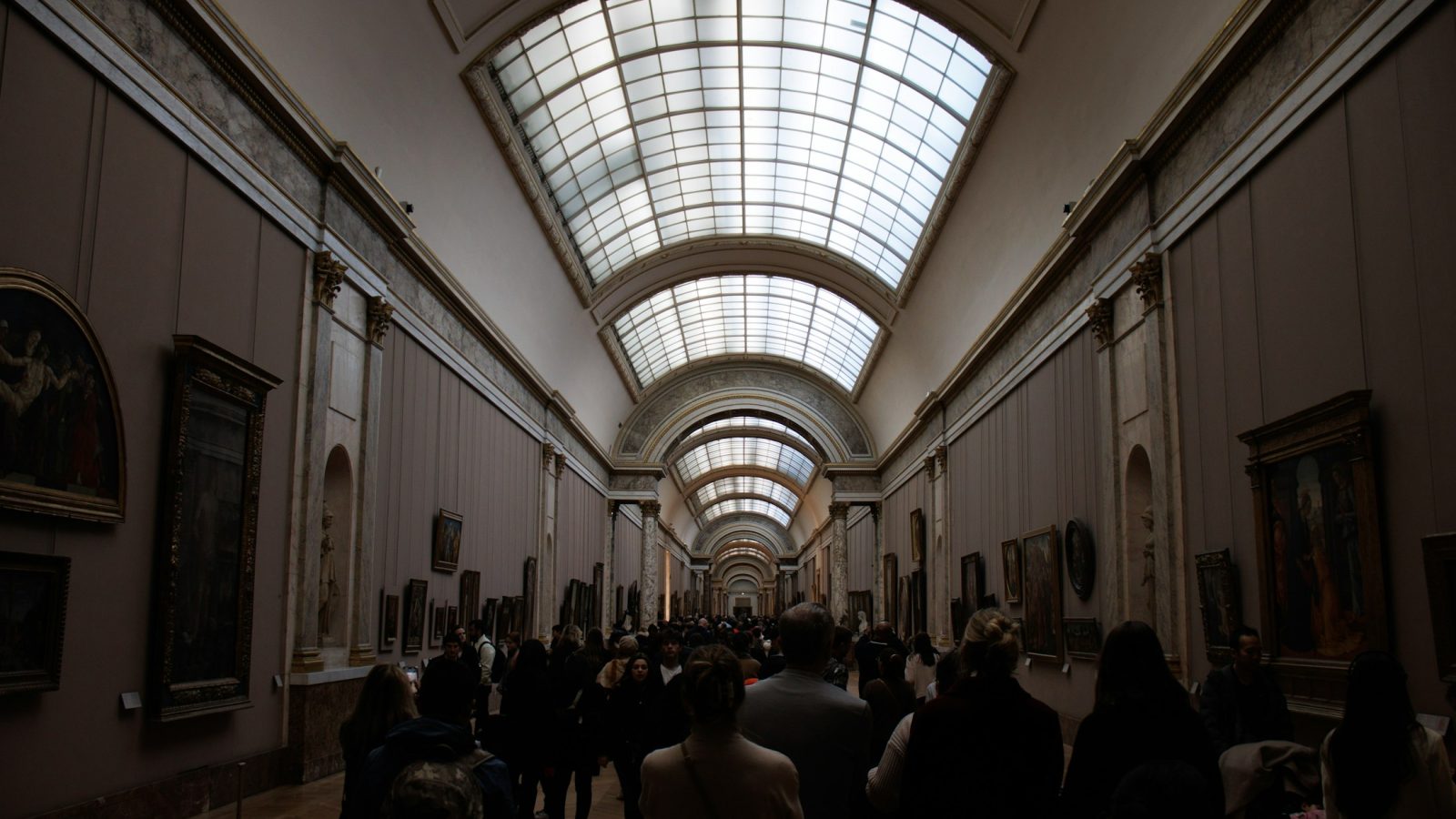 Besucherinnen und Besucher gehen durch eine lange Galerie mit Gemälden an den Wänden