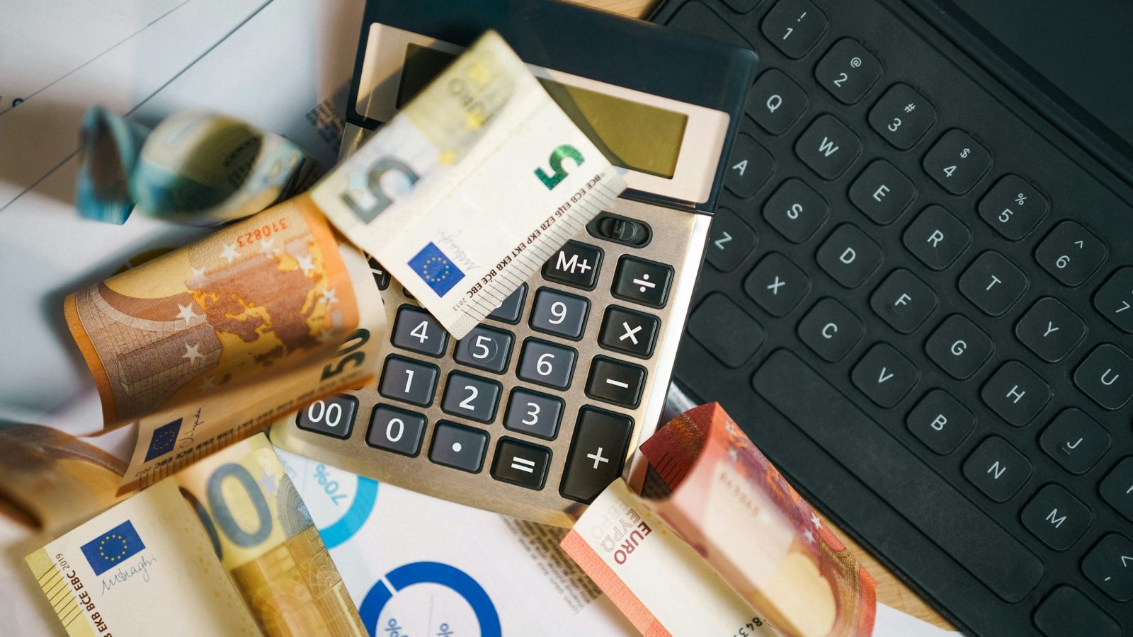 Taschenrechner, Euro-Banknoten und Tabellen mit Zahlen auf einem Schreibtisch