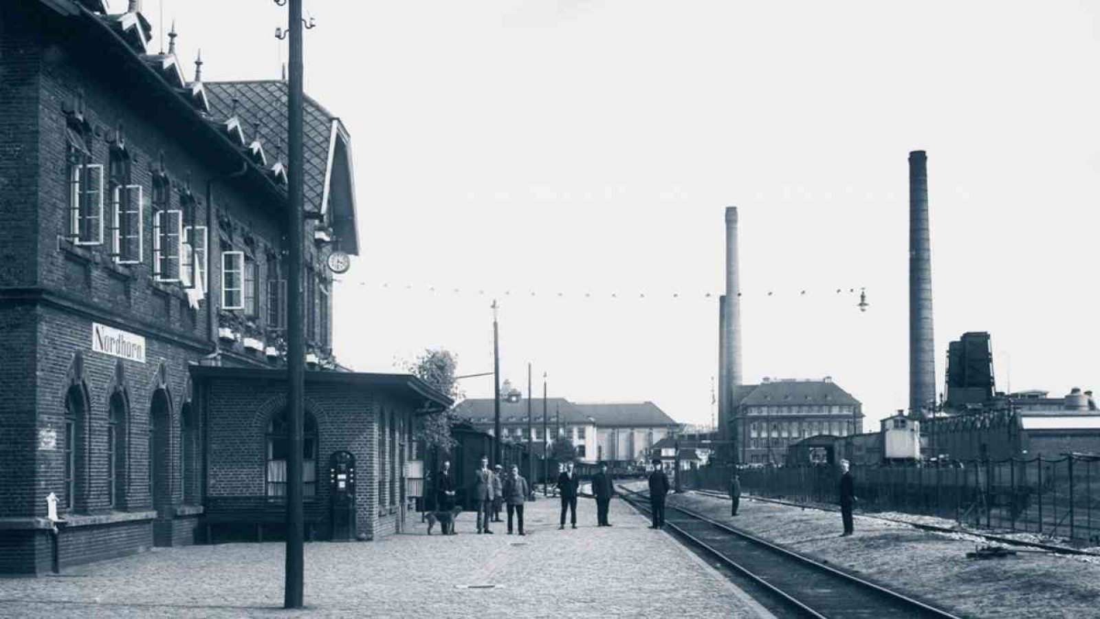 Bahnhofgebäude mit historischen Zügen und Personen auf dem Bahnsteig in Nordhorn.
