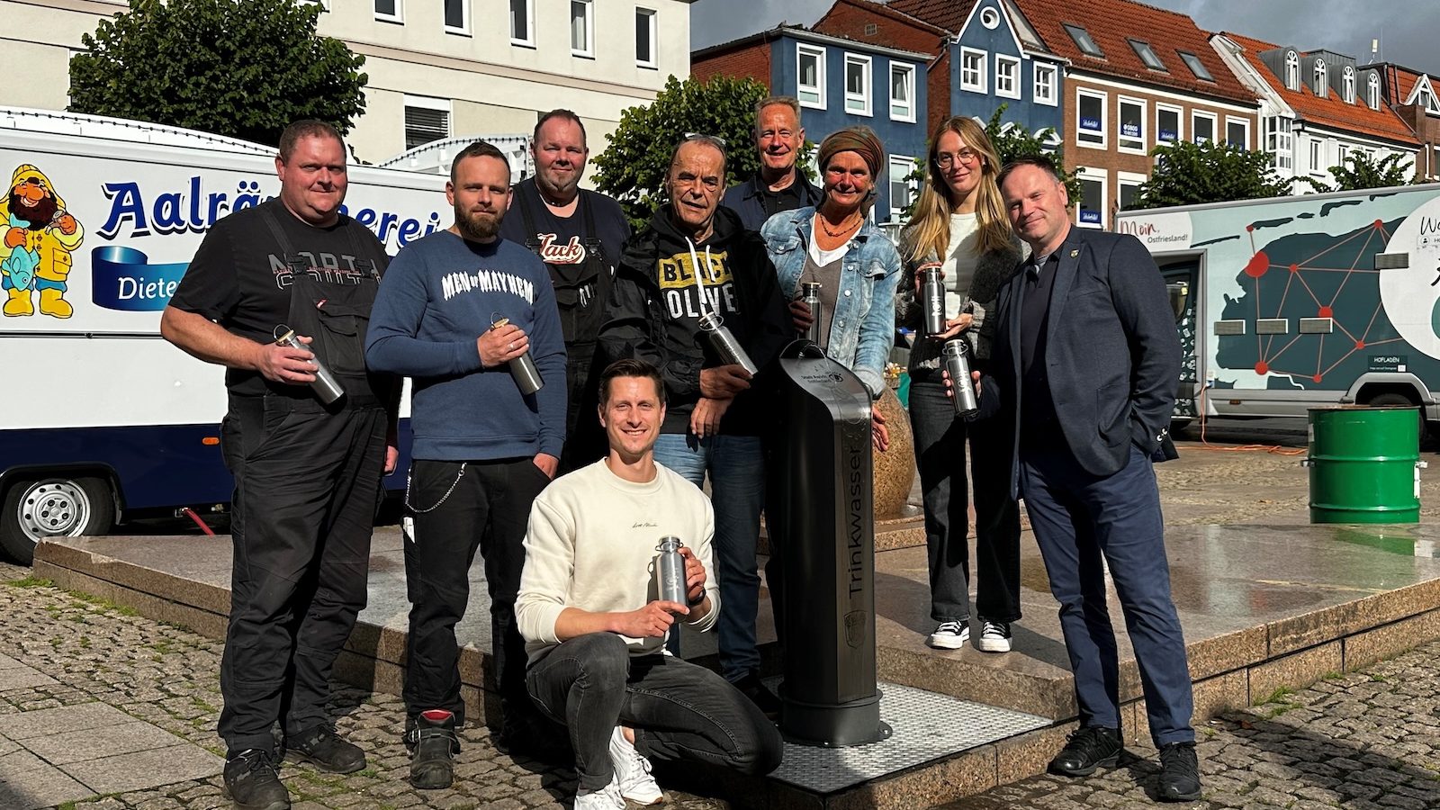 Mitarbeiter der Stadt Aurich und beteiligte Institutionen stehen bei der Einweihung um den neuen Trinkwasserbrunnen auf dem Auricher Marktplatz