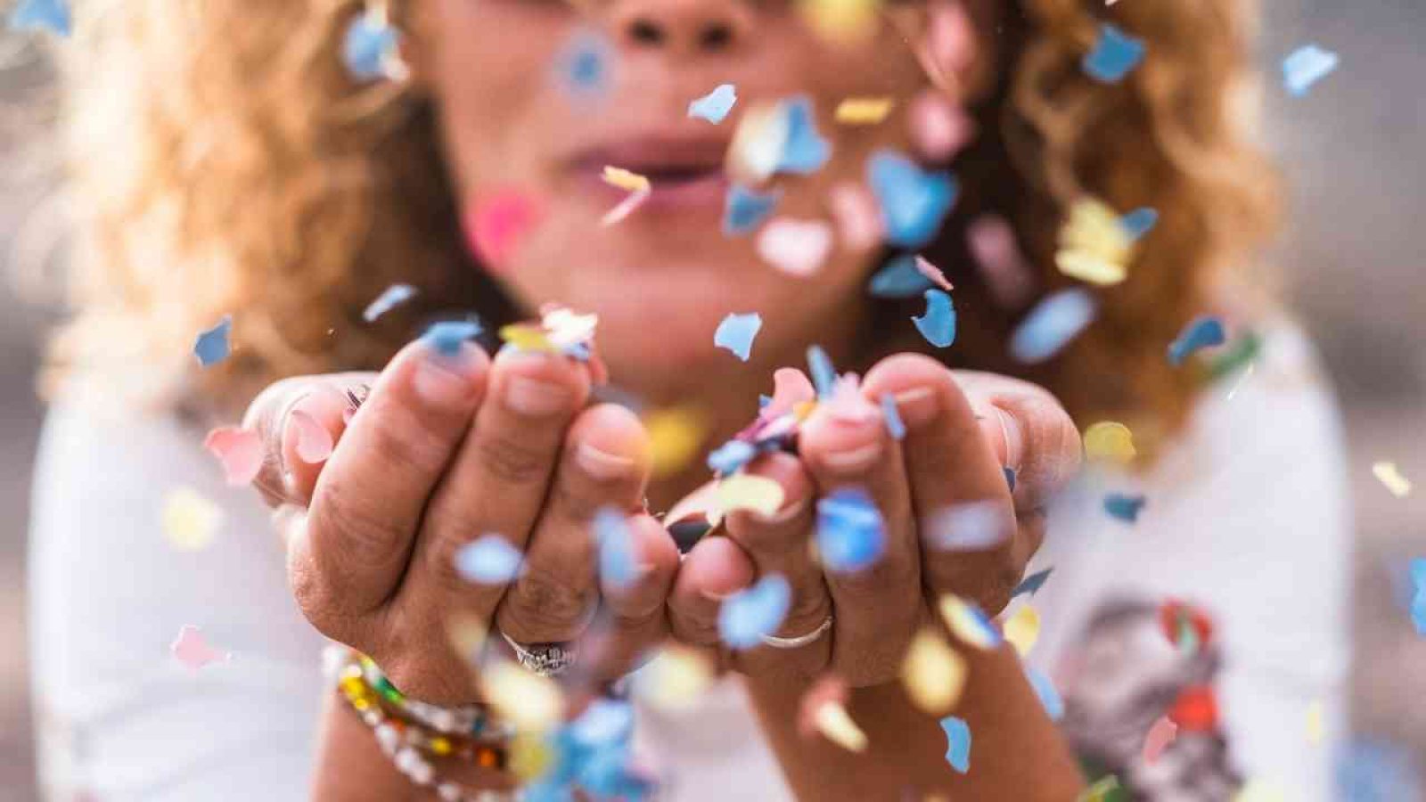 Frau pustet bunte Konfetti in die Luft, Feier und Freude im Fokus.