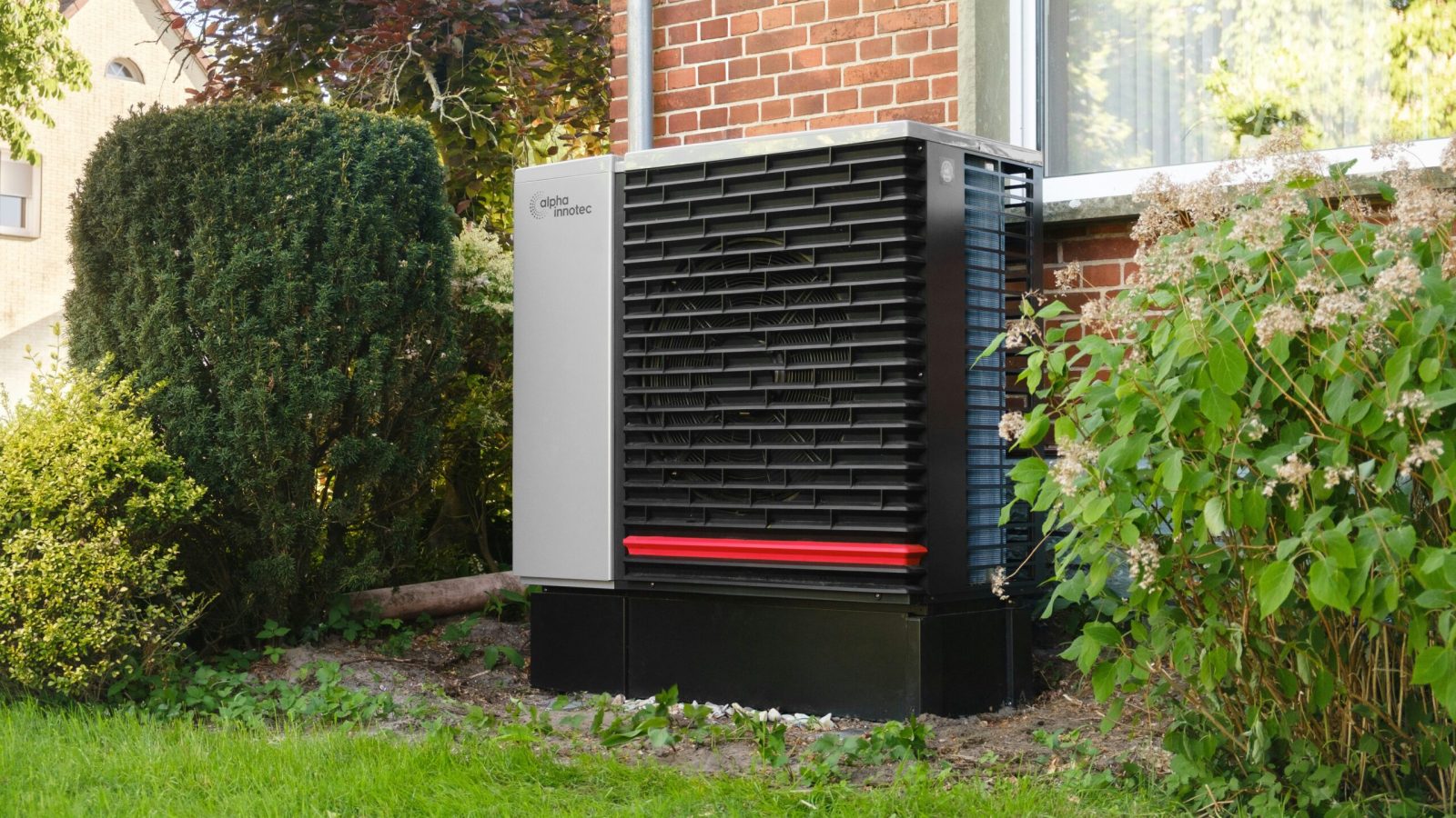 Moderne Wärmepumpe vor einem sanierten Wohnhaus