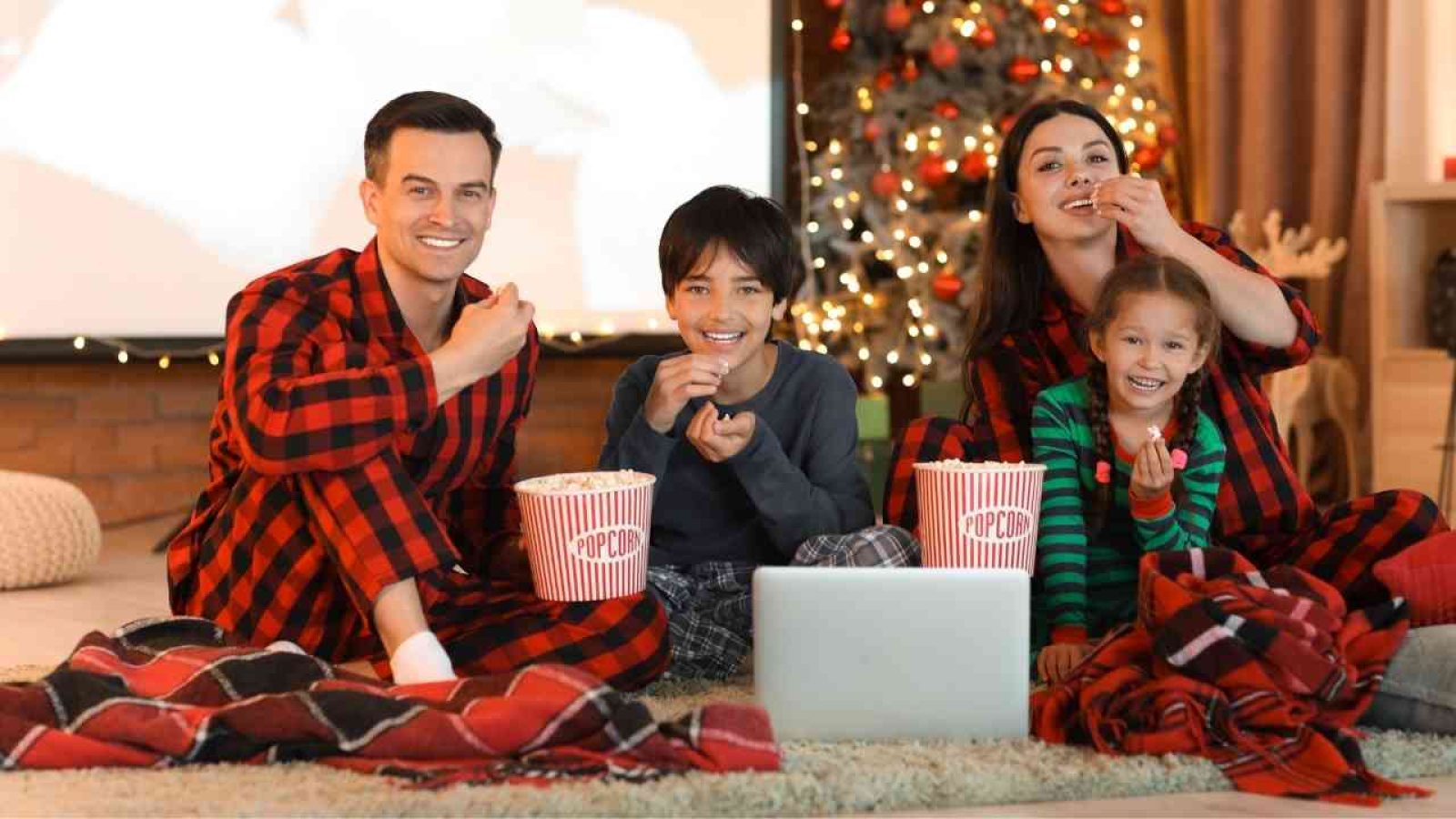 Familie in gestreiften Pyjamas, die Popcorn isst und einen Film schaut, während sie auf einem Teppich sitzt.