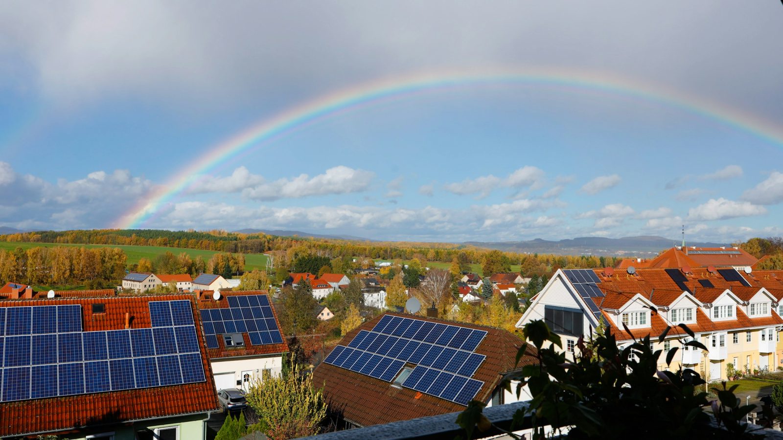 Mehrere Wohnhäuser mit Photovoltaikanlagen auf den Dächern, darüber ein Regenbogen