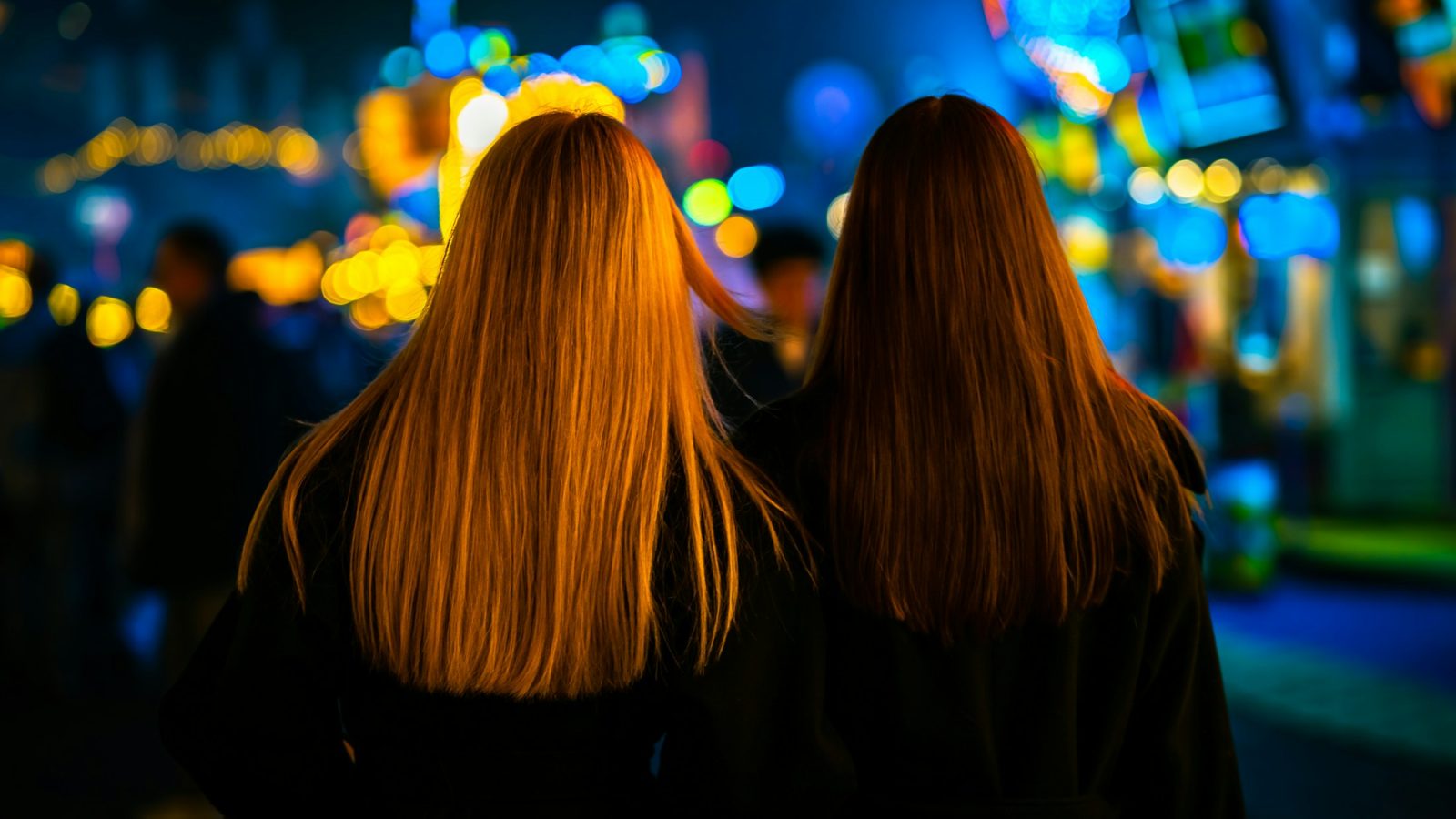 Zwei Frauen gehen abends durch eine beleuchtete Stadt