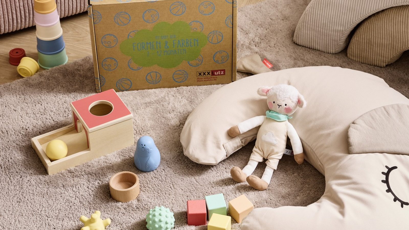 Bunte Spielzeuge und eine Babybox mit verschiedenen Spielzeugen auf einem Teppich in einem Innenraum.