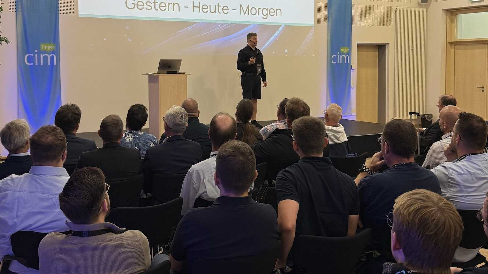 Redner auf der Bühne der cim lingen vor Publikum, im Hintergrund die Präsentationsleinwand und cim-Banner