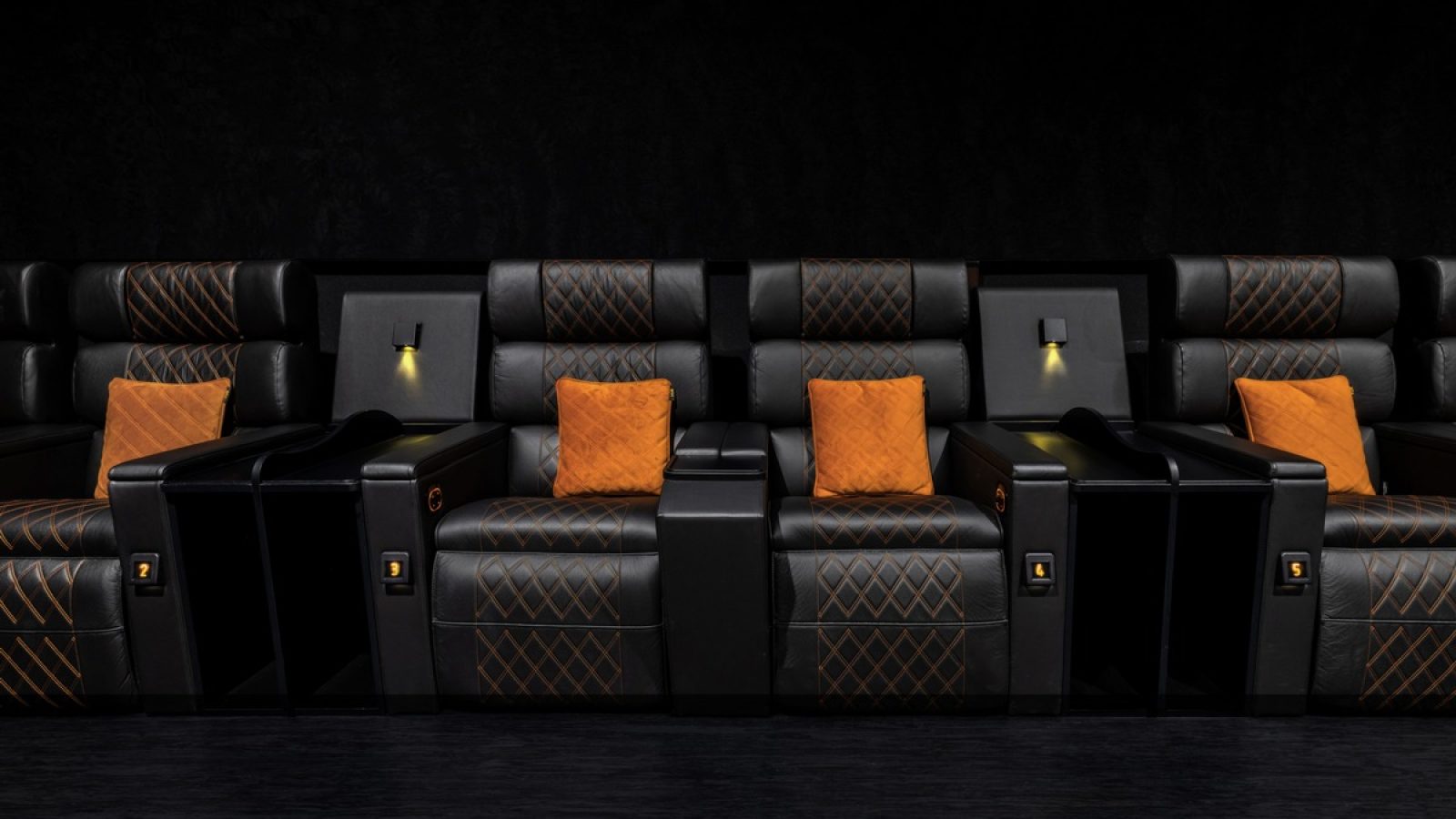 Schwarze Kinosessel mit orangefarbenen Kissen und integrierter Beleuchtung in einem modernen Kinosaal.