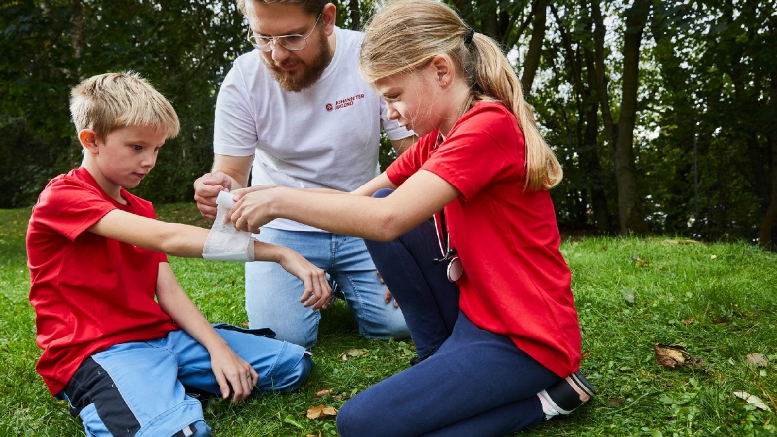 Zwei Kinder üben das Anlegen eines Verbands mit einem Jugendgruppenleiter der Johanniter Jugend. / Weiterer Text über ots und www.presseportal.de/nr/14240 / Die Verwendung dieses Bildes für redaktionelle Zwecke ist unter Beachtung aller mitgeteilten Nutzungsbedingungen zulässig und dann auch honorarfrei. Veröffentlichung ausschließlich mit Bildrechte-Hinweis.