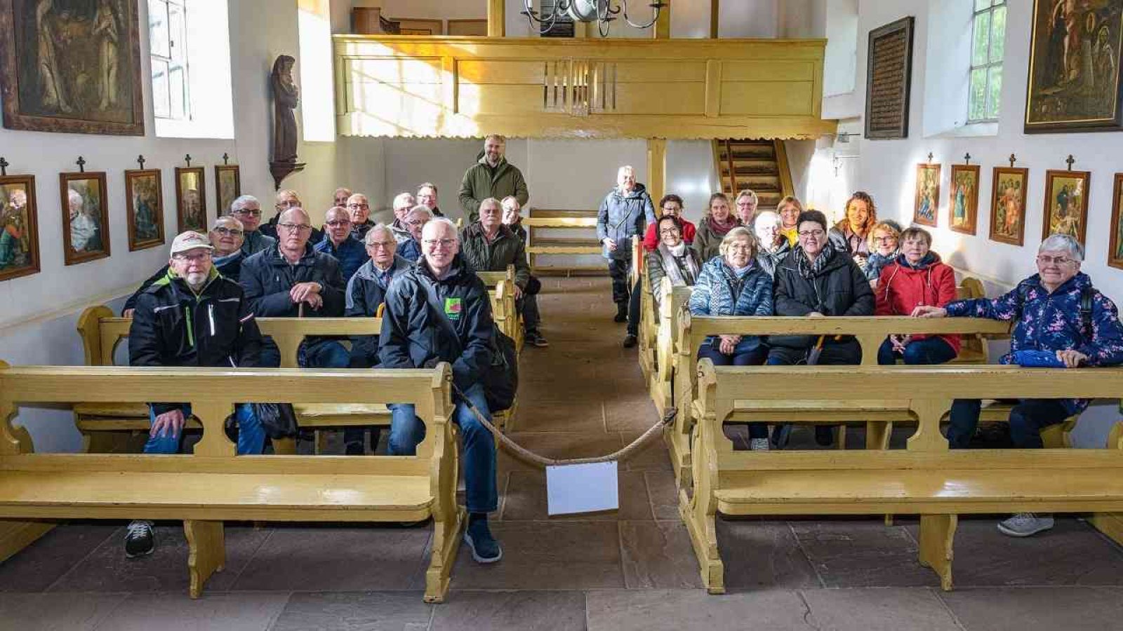 Gruppe von Menschen in einer Kirche, die auf Holzbänken sitzen und in die Kamera schauen.