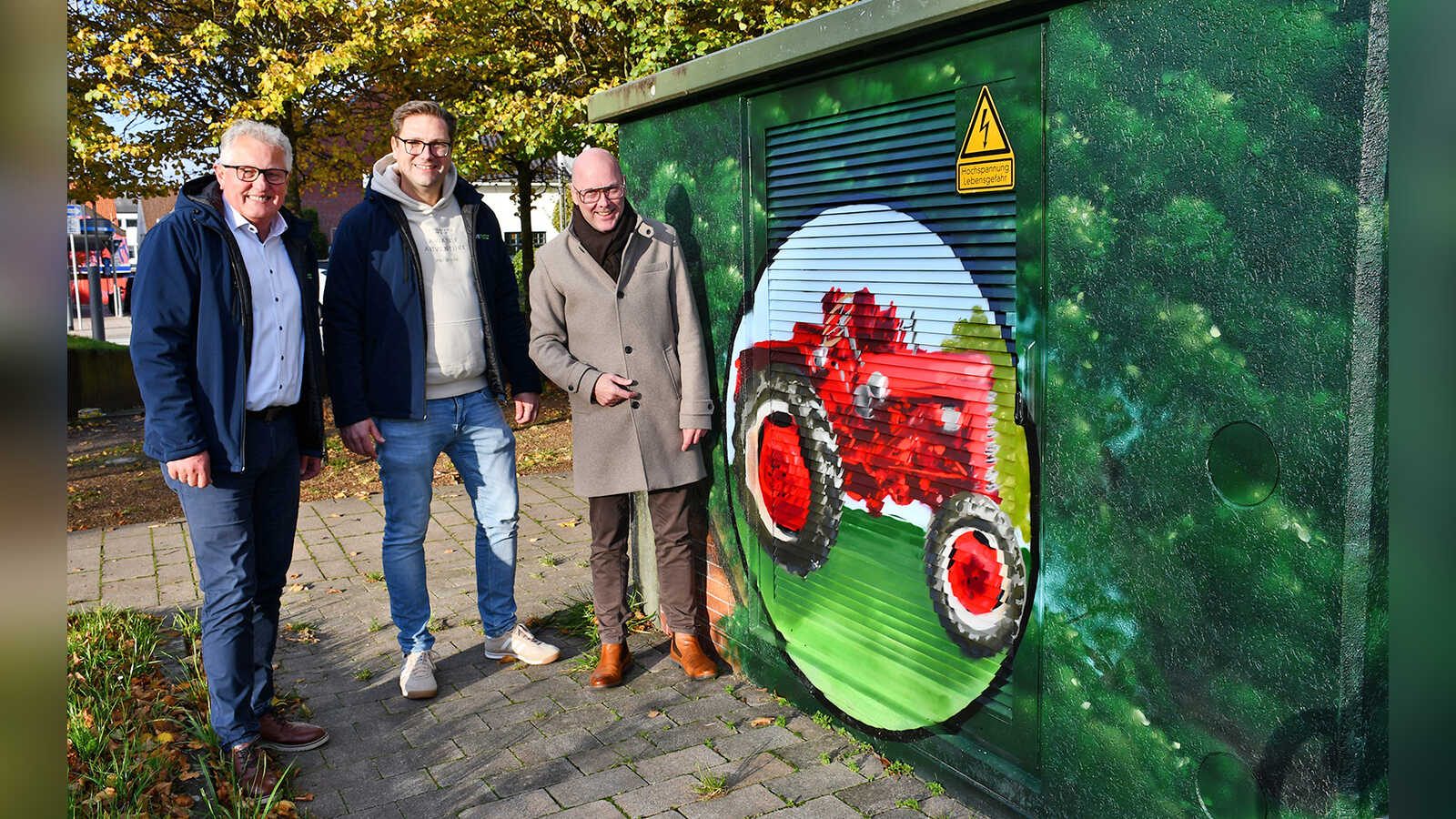 Thomas Lüllmann, Gerd Niemann und Bürgermeister Neidhard Varnhorn vor einer Trafostation mit einem gemalten roten Trecker
