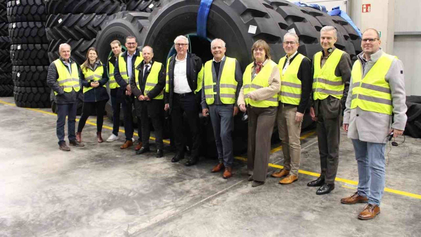 Gruppe von Personen in Sicherheitswesten steht vor großen Reifen in einem Lagerhaus.