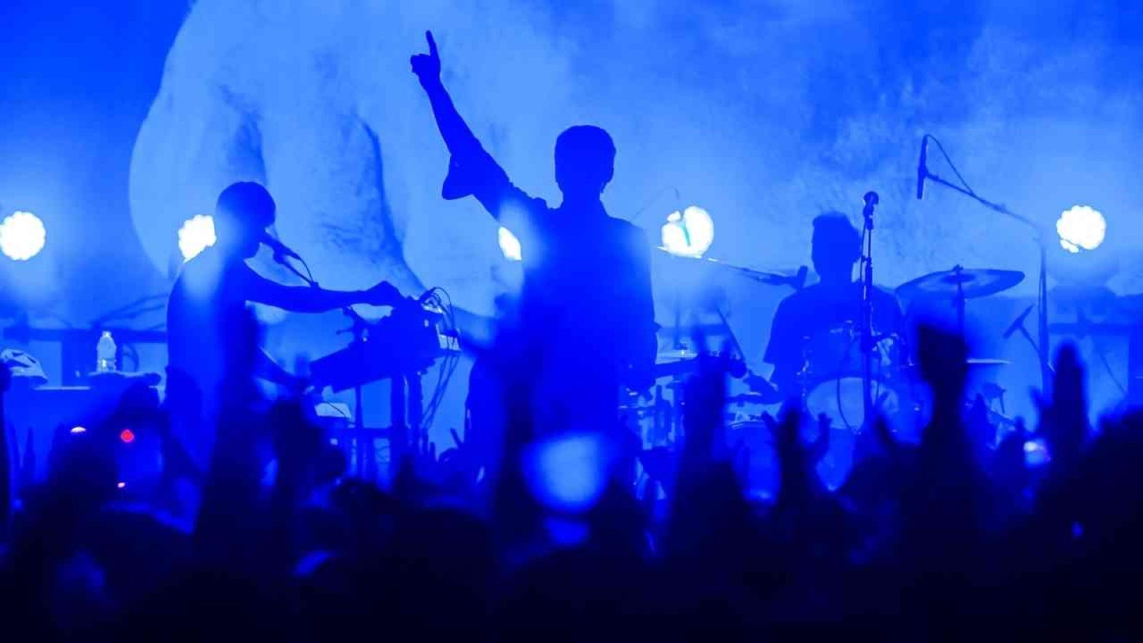 Silhouette von Musikern auf einer Bühne mit blauer Beleuchtung während eines Live-Konzerts.