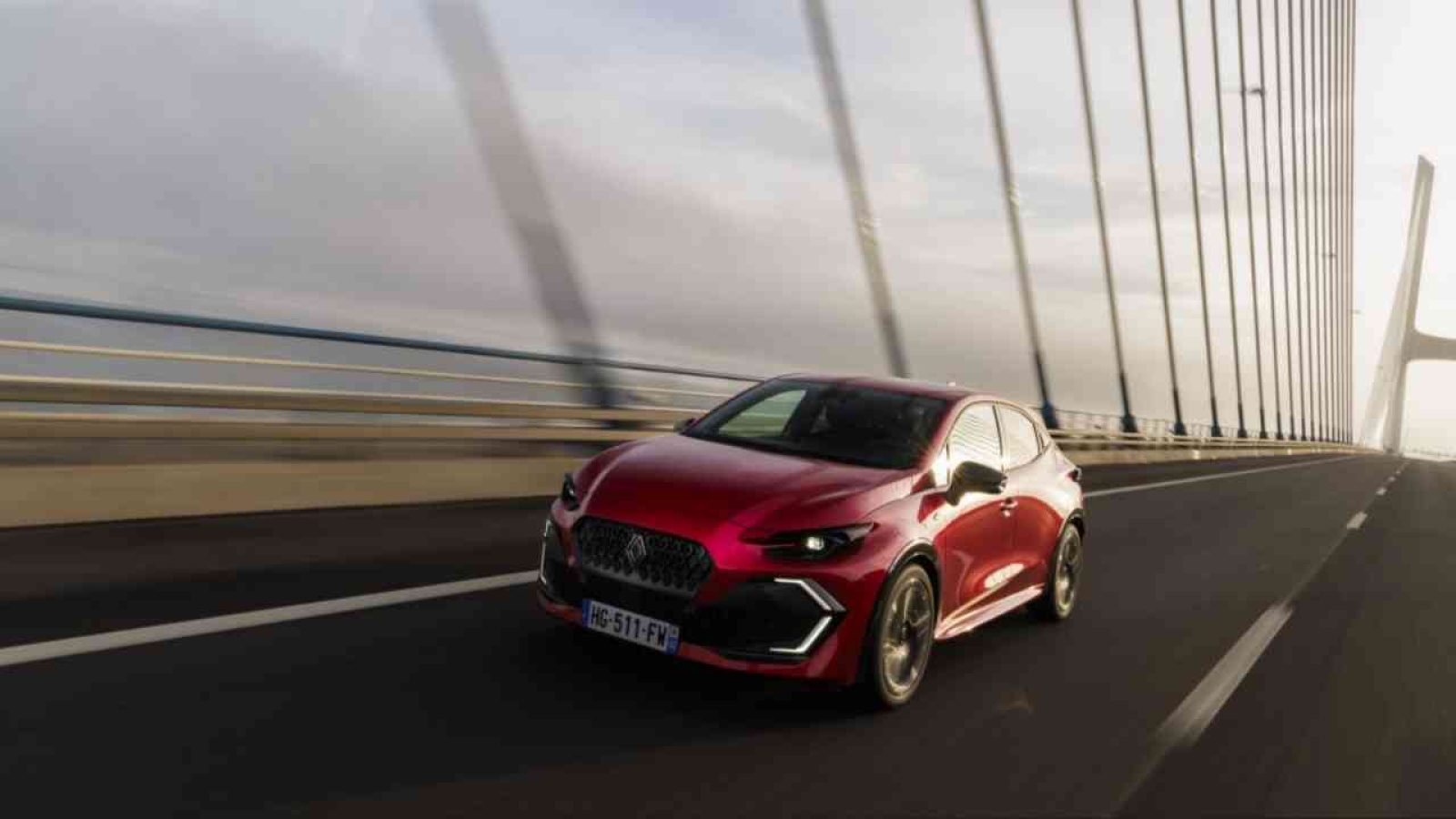 Roter Renault Clio fährt auf einer Brücke mit modernen Architekturmerkmalen im Hintergrund.