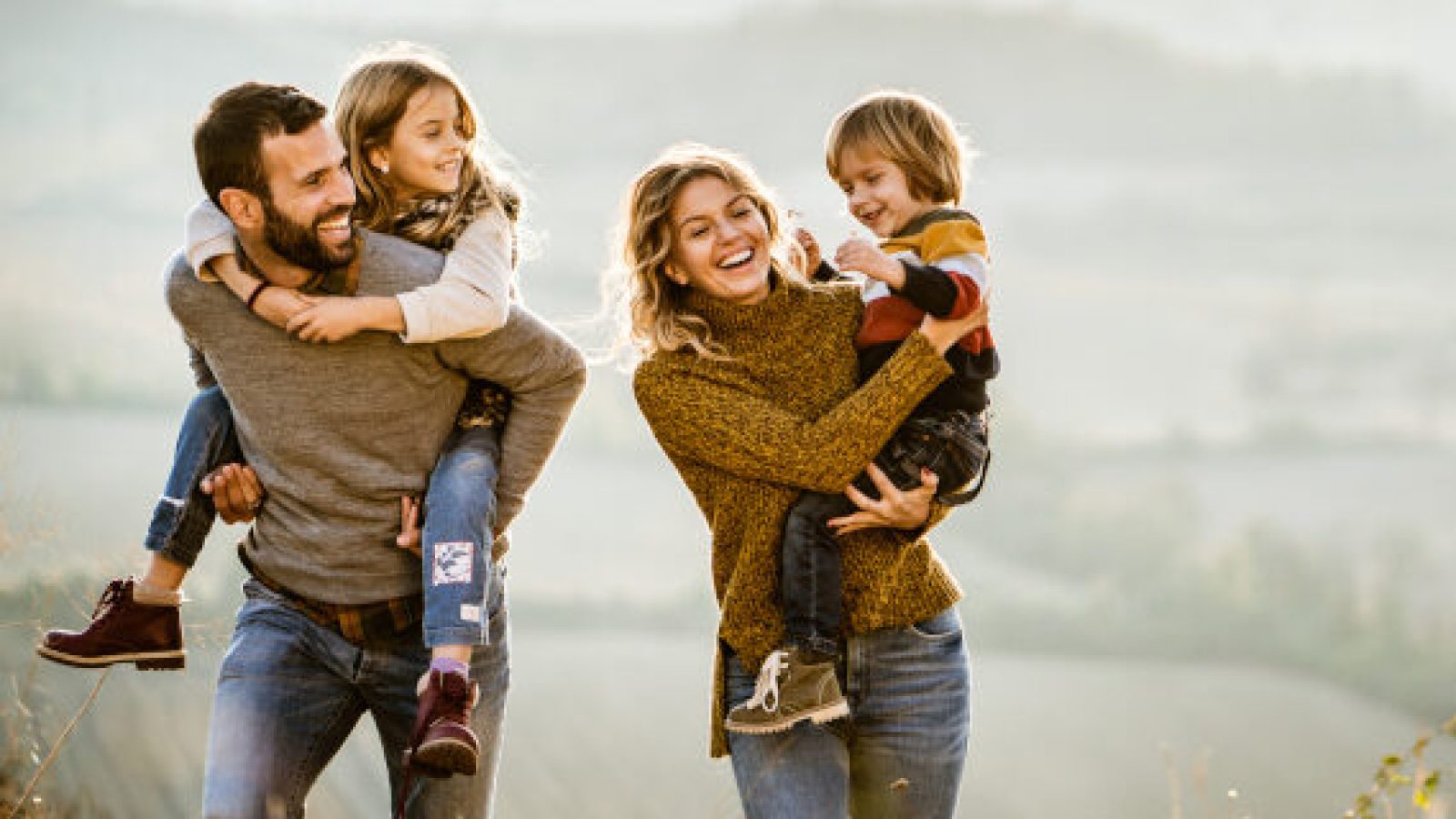 Familie mit zwei Kindern, die im Freien lachen und spielen, während sie auf einem Hügel stehen.