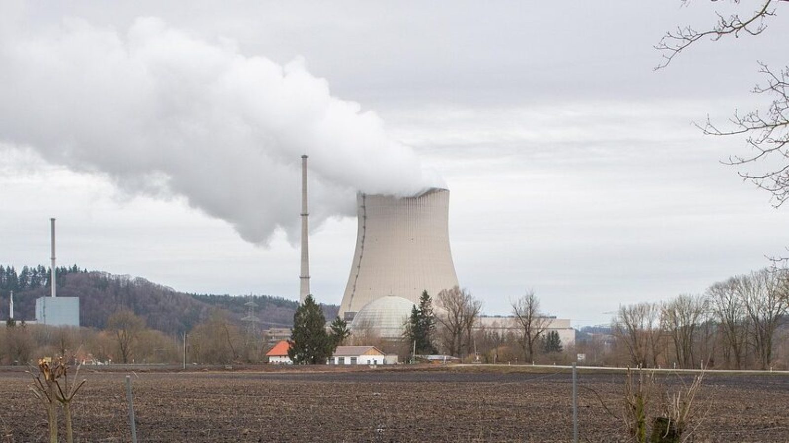 Kernkraftwerk mit Kühlturm und Rauchabzug, umgeben von landwirtschaftlicher Fläche.
