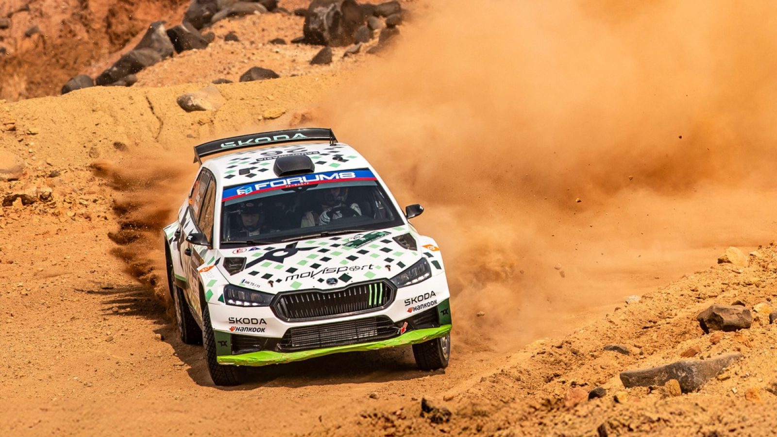 Rennwagen von Škoda, der durch eine sandige Strecke bei einem Rallye-Event fährt und Staub aufwirbelt.