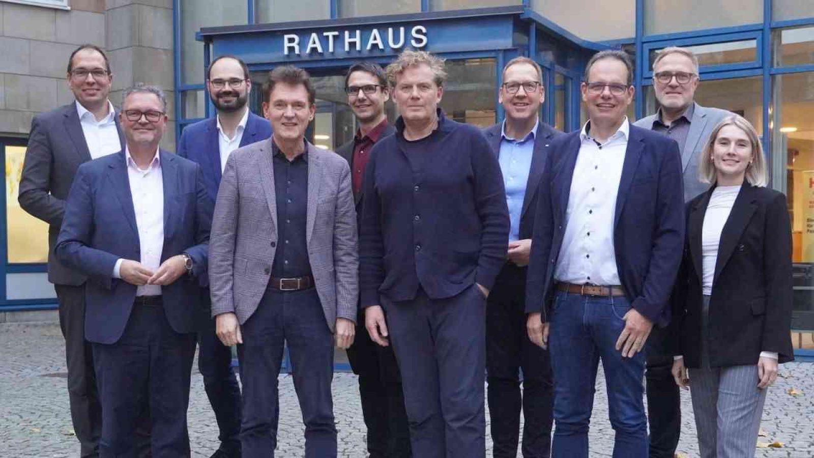 Gruppe von Personen vor dem Rathaus, die in formeller Kleidung stehen und in die Kamera schauen.