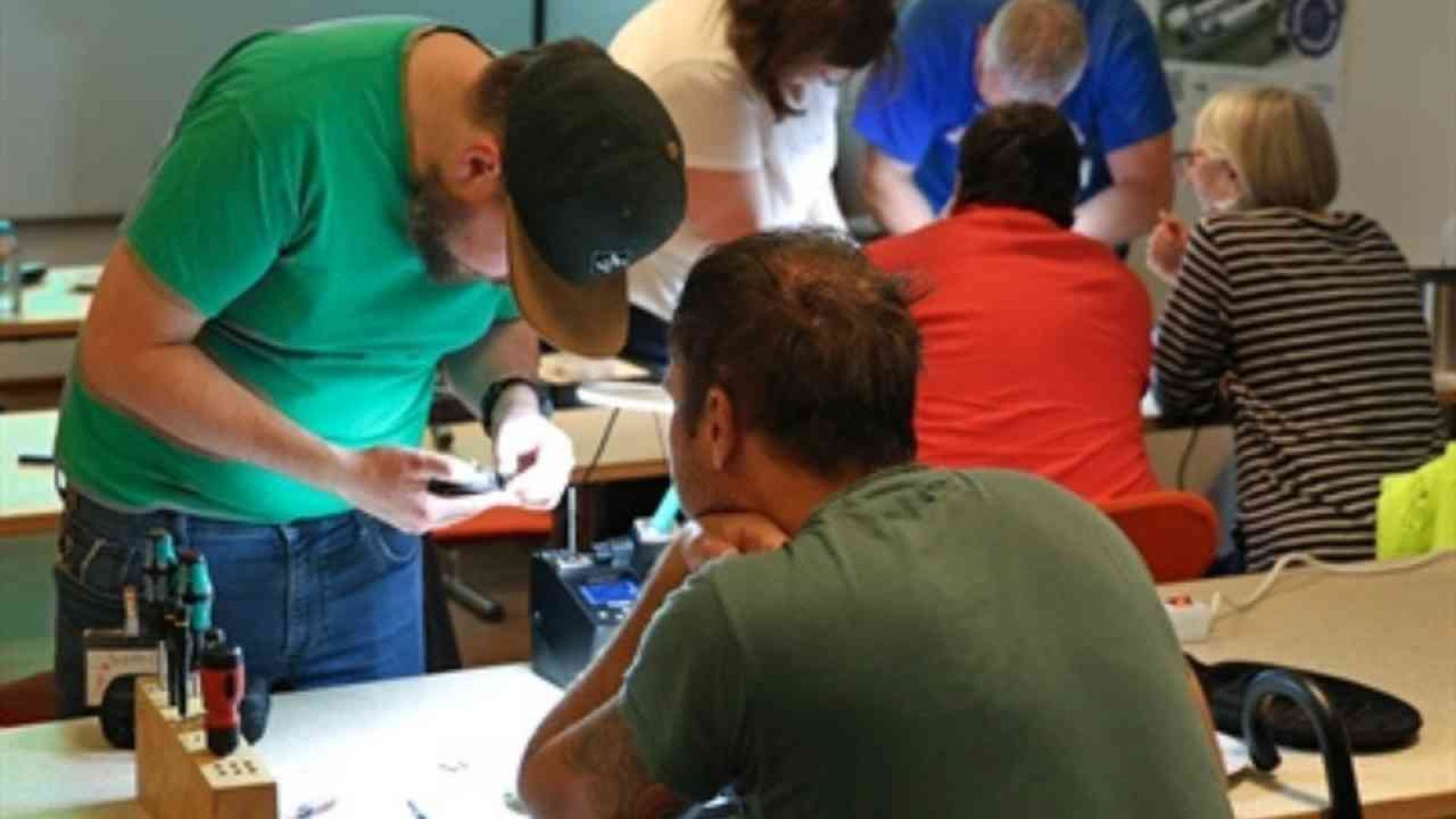 Personen arbeiten an Elektrogeräten in einem Reparaturcafé in Münster, um defekte Geräte zu reparieren.