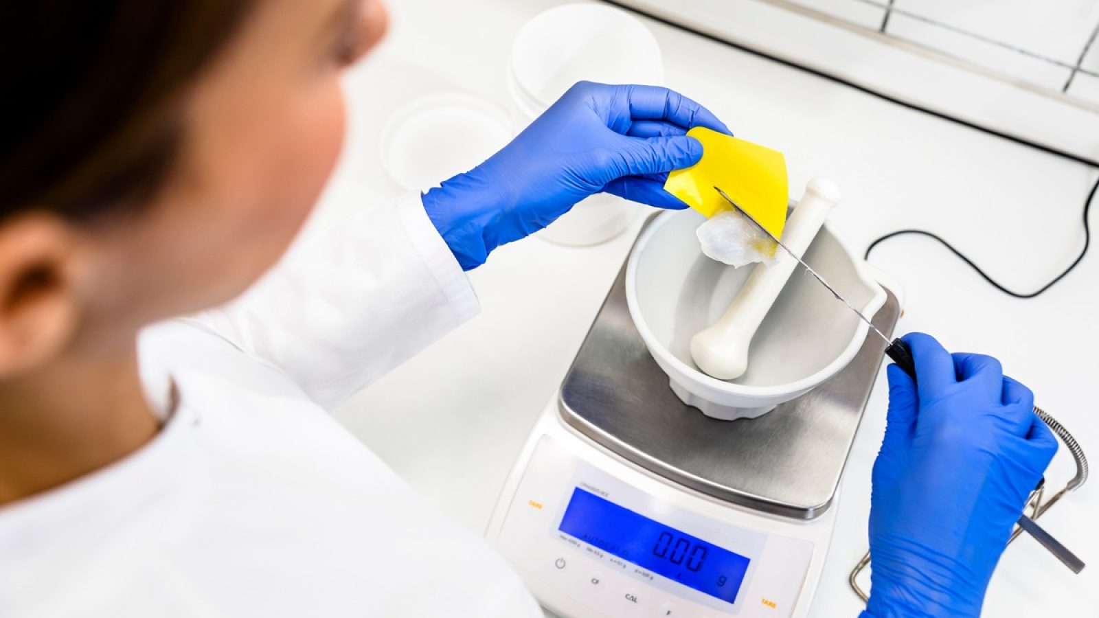 Laborantin wiegt Zutaten mit einer digitalen Waage in einem Mörser für chemische Analysen.