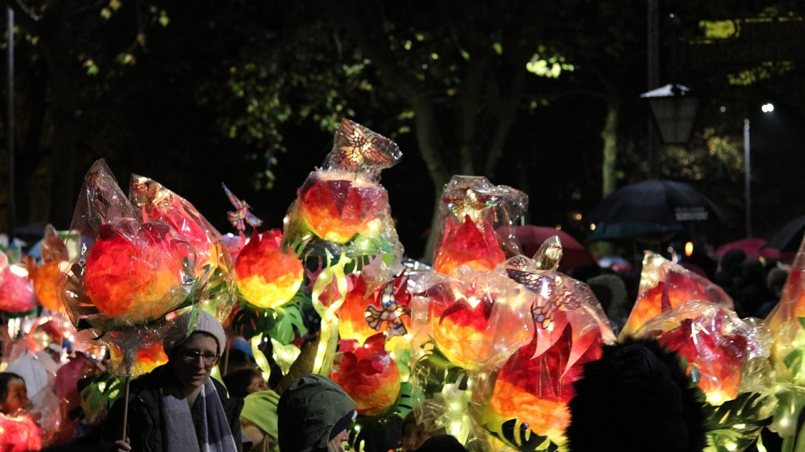 Leuchtende Blumen aus transparentem Material mit bunten Blüten in einer Menschenmenge bei einer Veranstaltung.