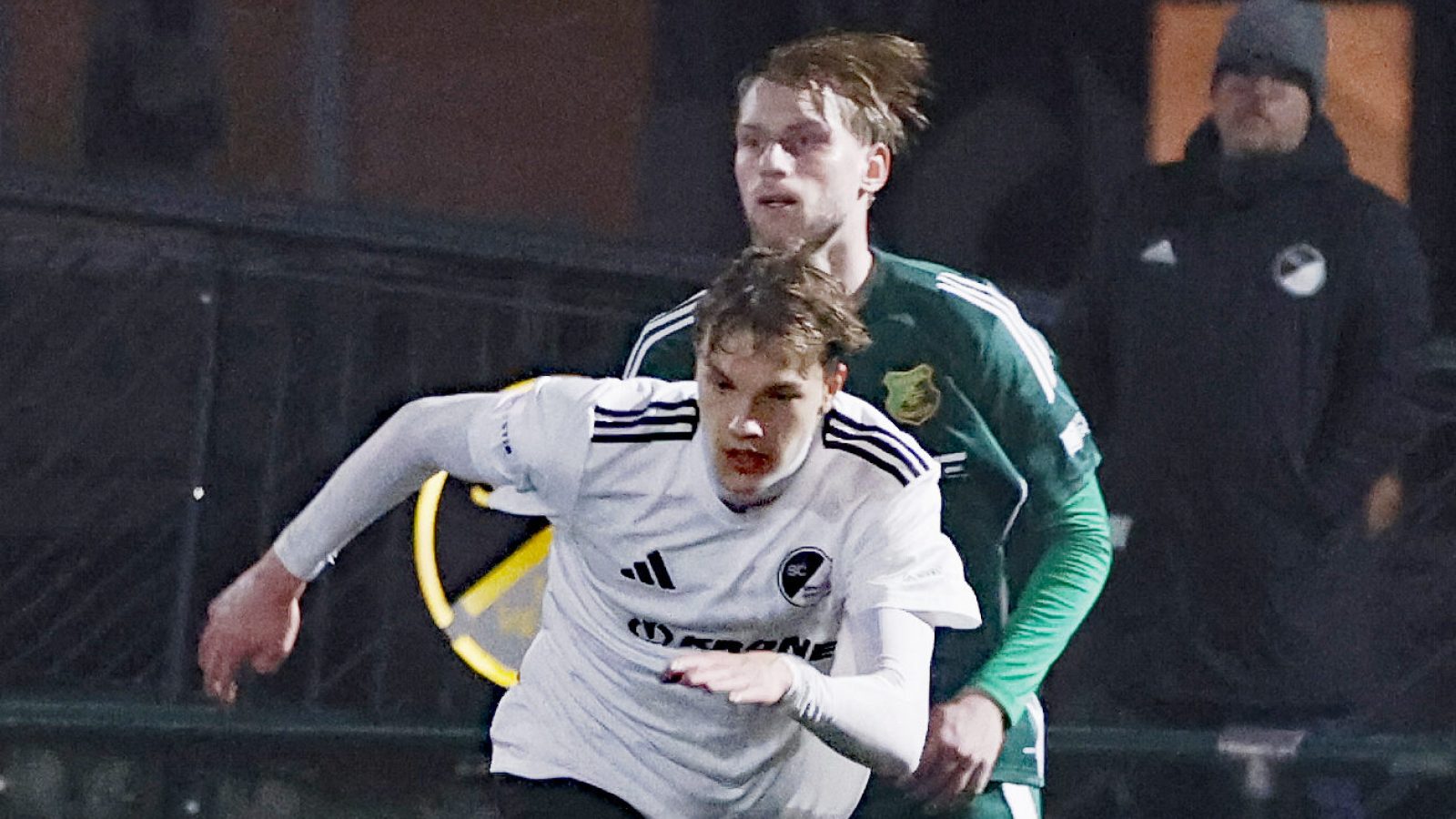 Zwei Fußballspieler in Aktion während eines Spiels, einer trägt ein weißes Trikot mit schwarzem Logo.