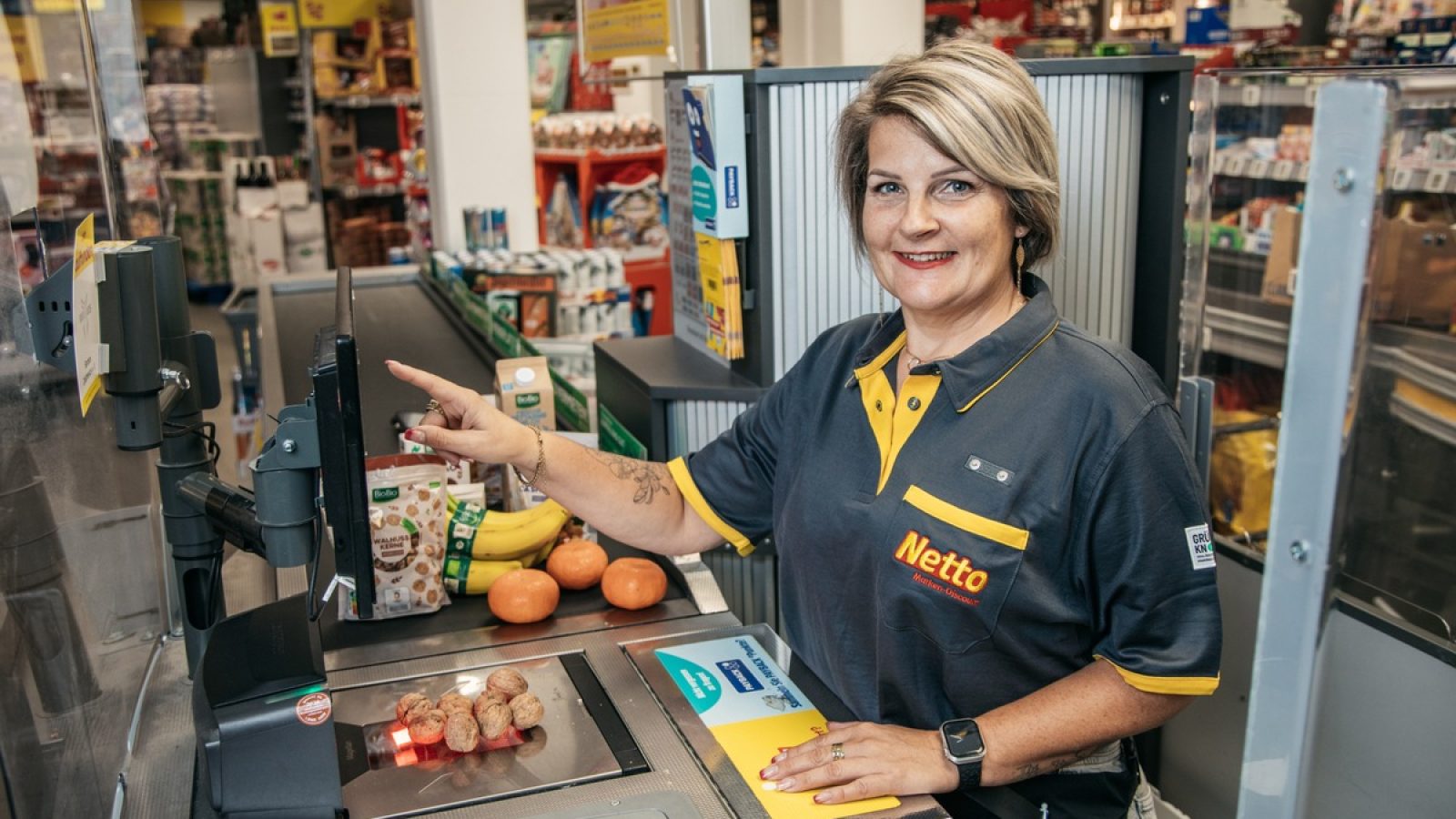 Kassiererin bei Netto, die an einer Selbstbedienungskasse arbeitet und einen Artikel scannt.
